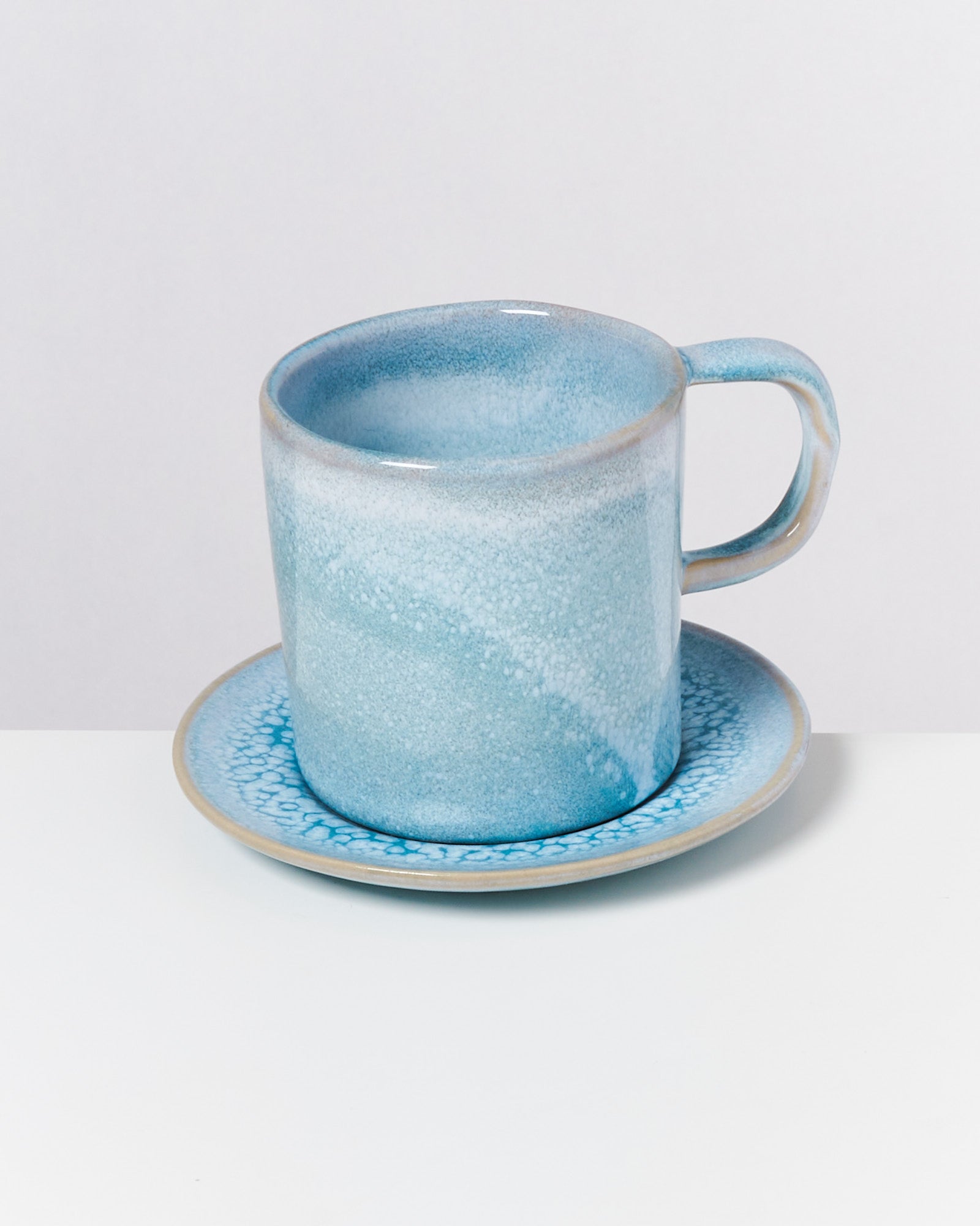Blaue Keramiktasse mit passender Untertasse auf weißem Hintergrund.