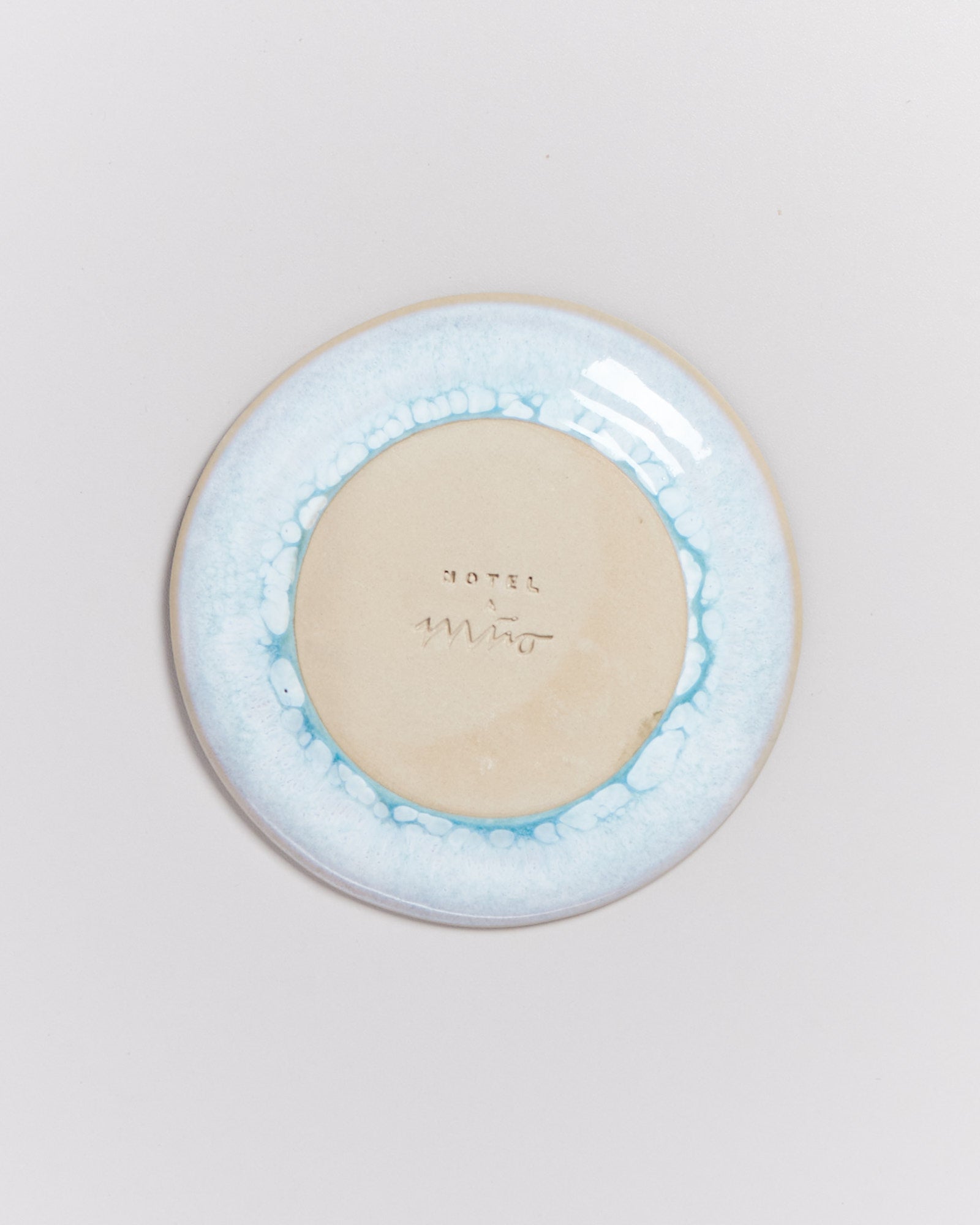 Runde Keramikplatte mit hellblauem Rand und der Aufschrift "HOTEL" und einer Signatur in der Mitte.