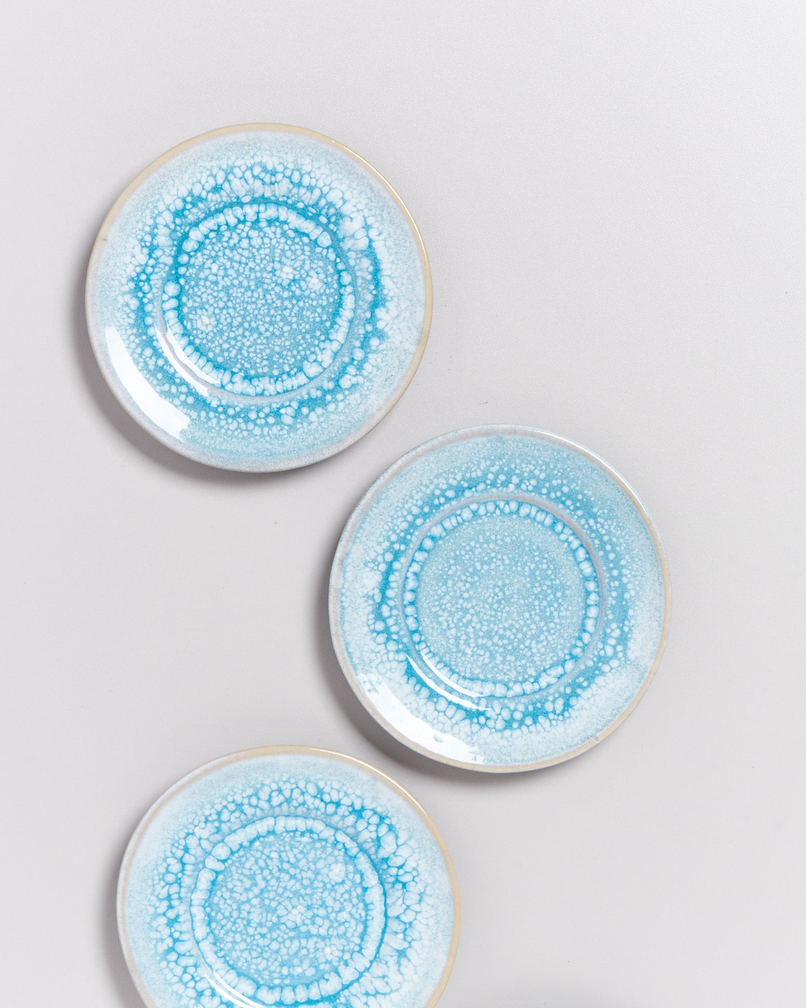 Drei runde Teller mit blauer, strukturiert wirkender Glasur auf hellem Hintergrund.