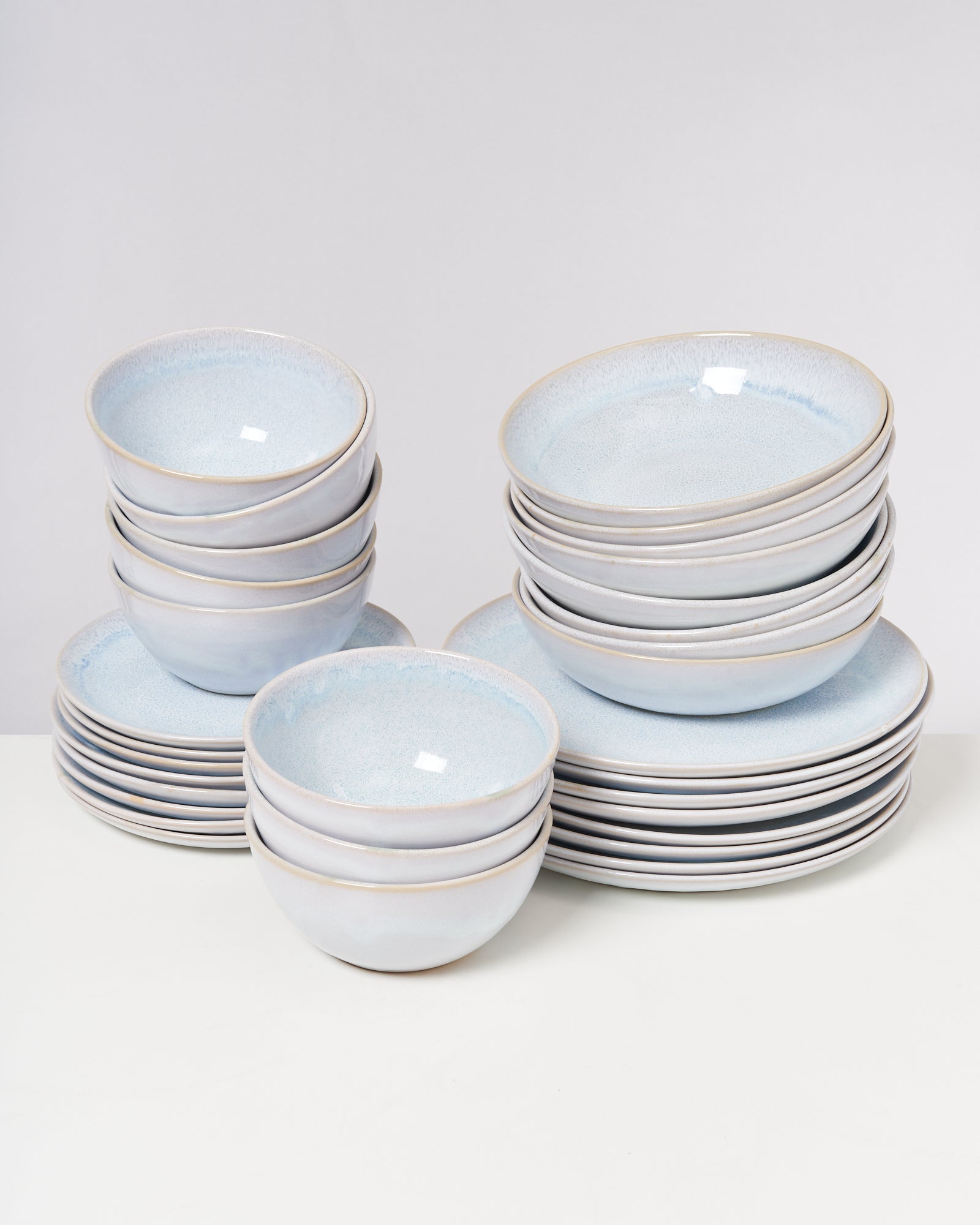 Stapelweise weiße Keramikschalen und Teller mit leicht bläulichem Schimmer auf einem weißen Hintergrund.
