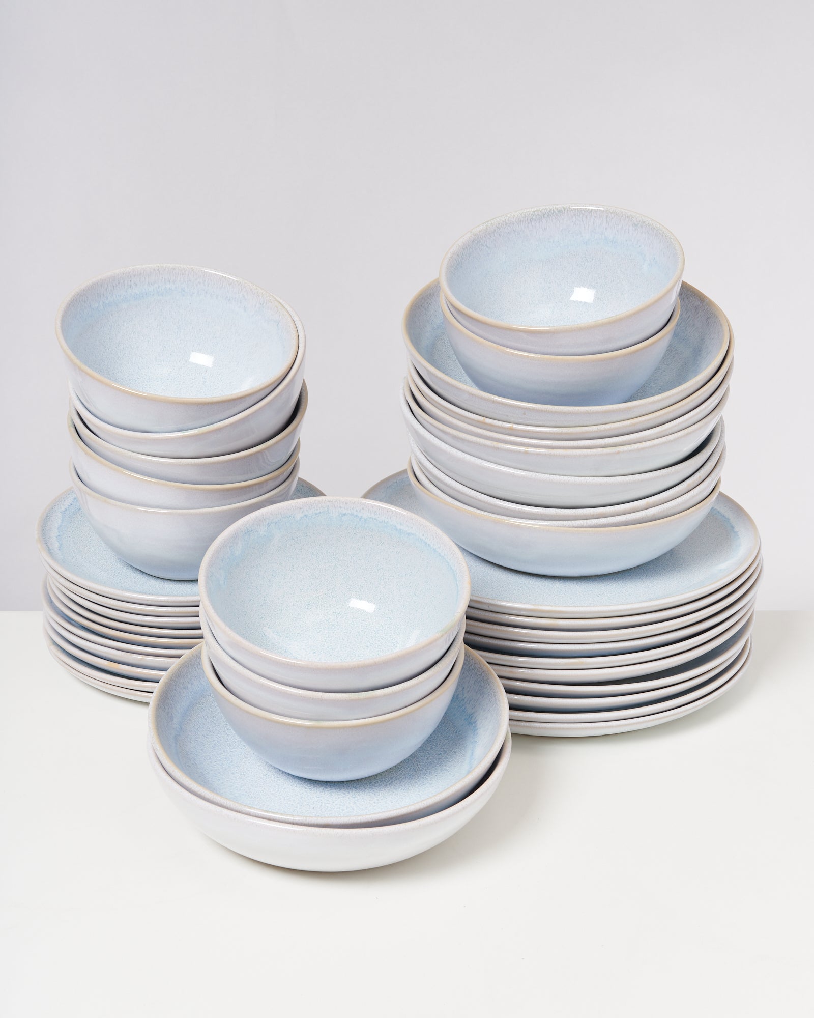 Gestapelte blaue Schüsseln und Teller auf einem weißen Tisch vor grauem Hintergrund.