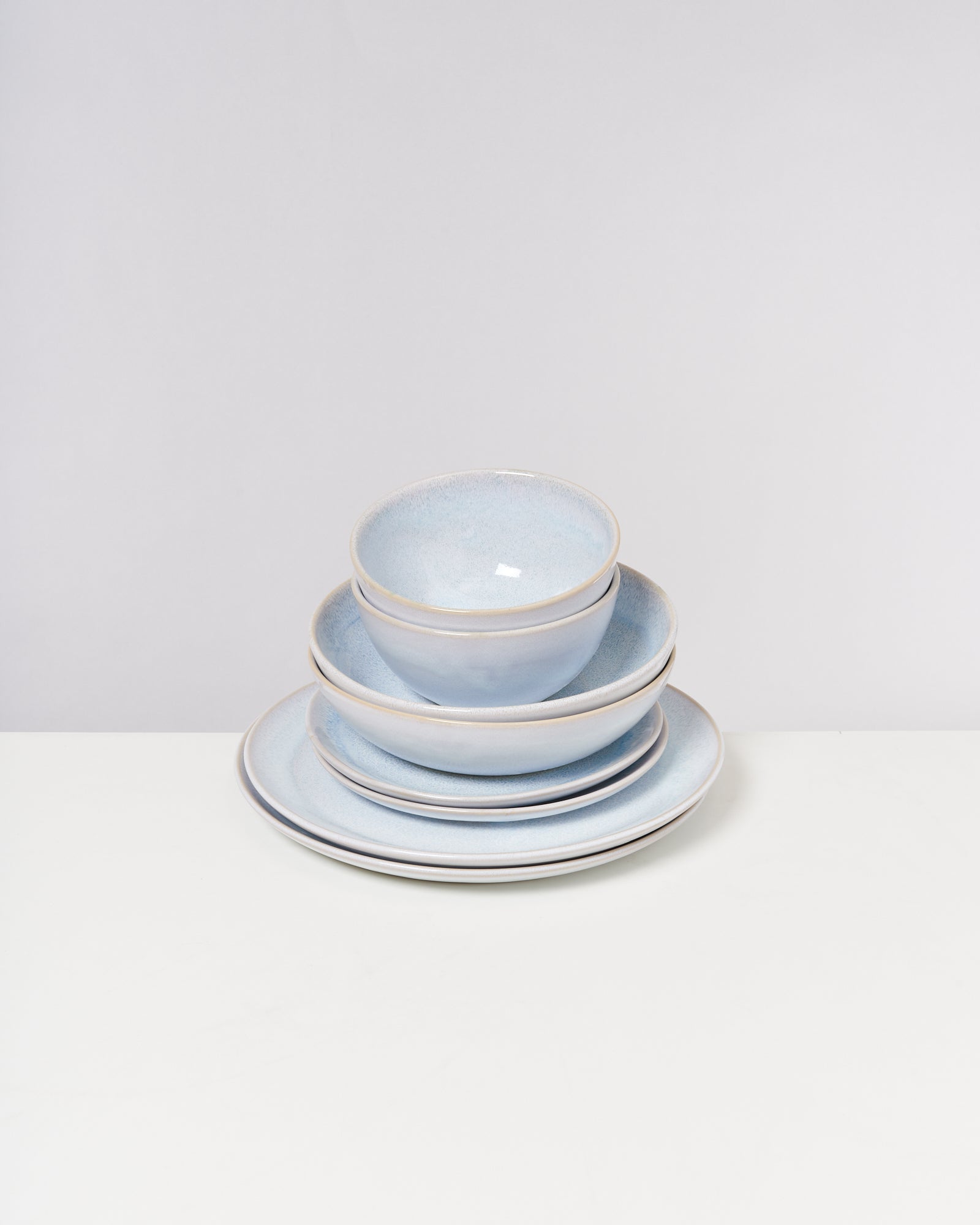 Ein Stapel hellblauer Keramikteller und -schalen auf einem weißen Tisch vor einem grauen Hintergrund.