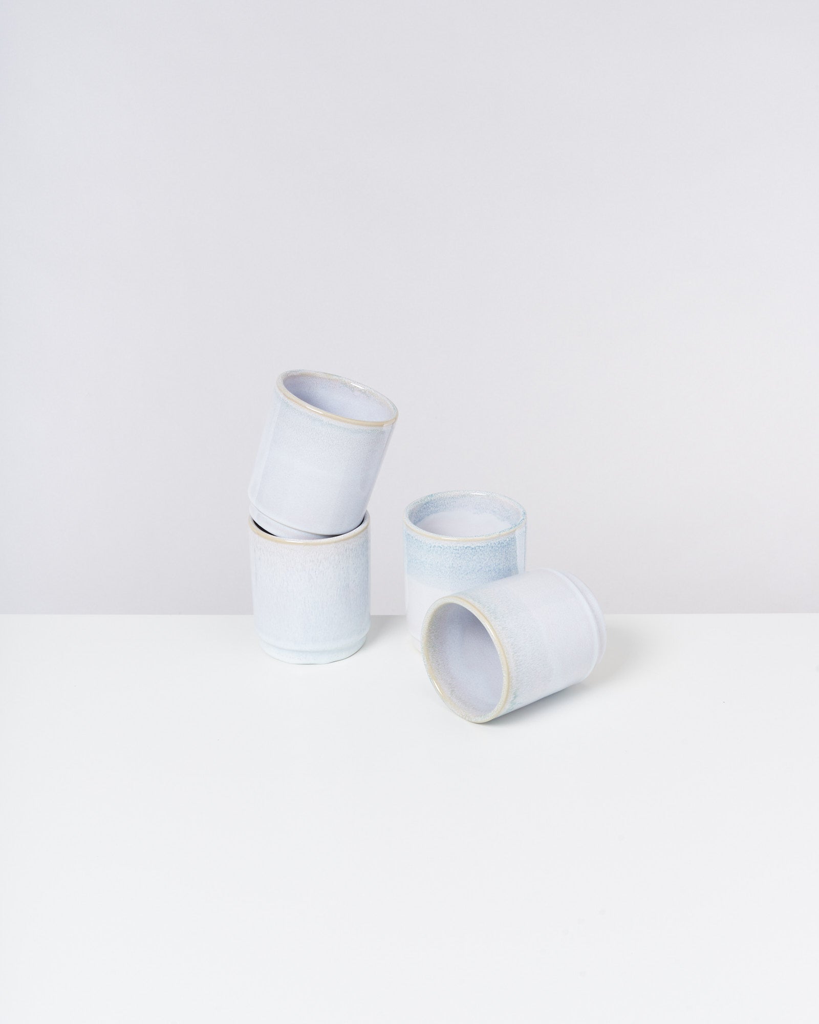 Vier weiße Keramikbecher stehen auf einem weißen Tisch, zwei davon sind übereinander gestapelt.