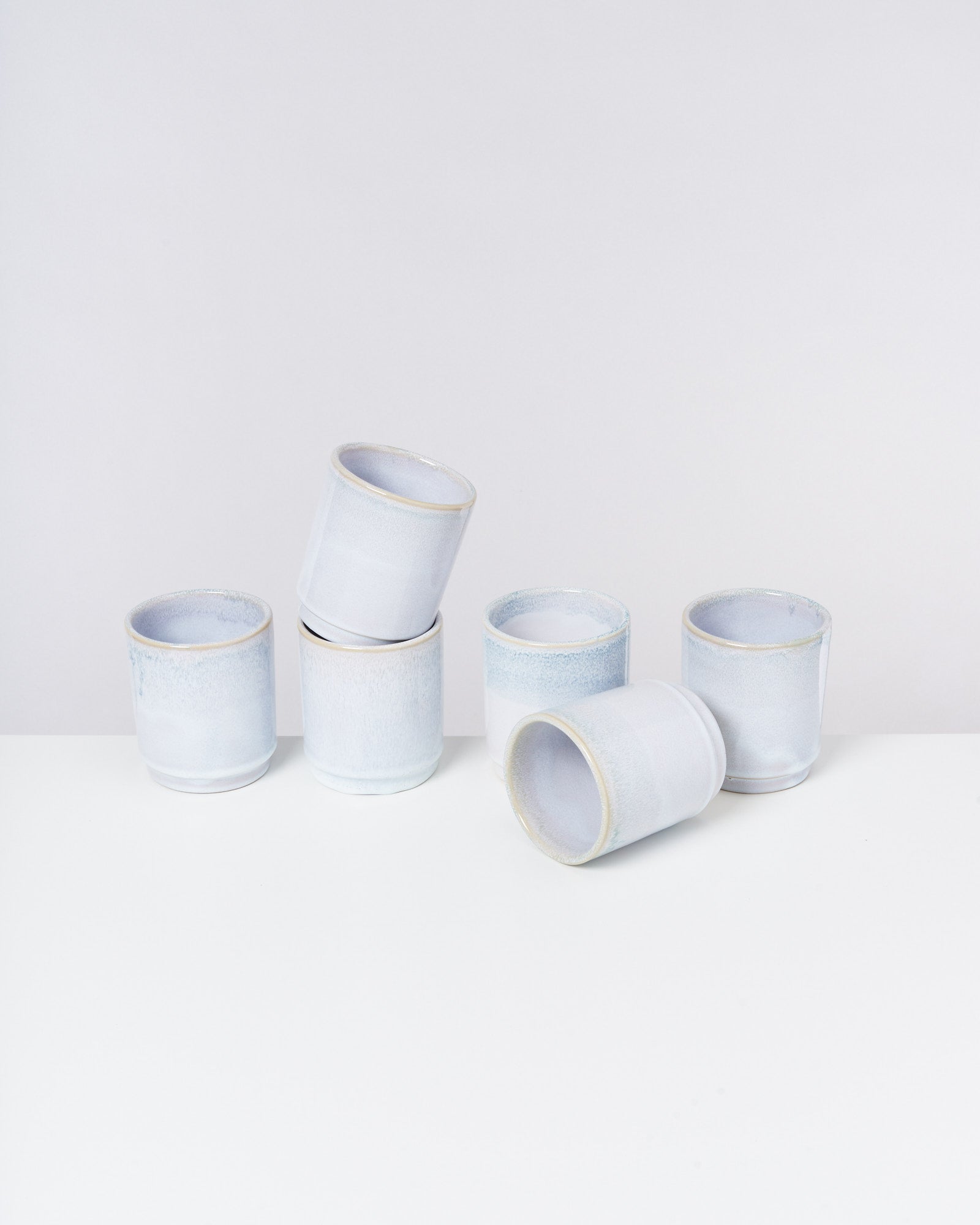 Sechs blaue Keramiktassen auf einer weißen Fläche, eine davon liegt auf der Seite.