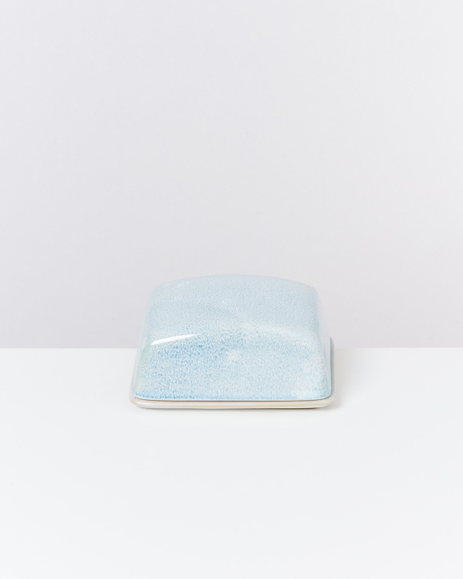 Hellblaue Keramikbutterdose mit Deckel auf weißem Hintergrund.