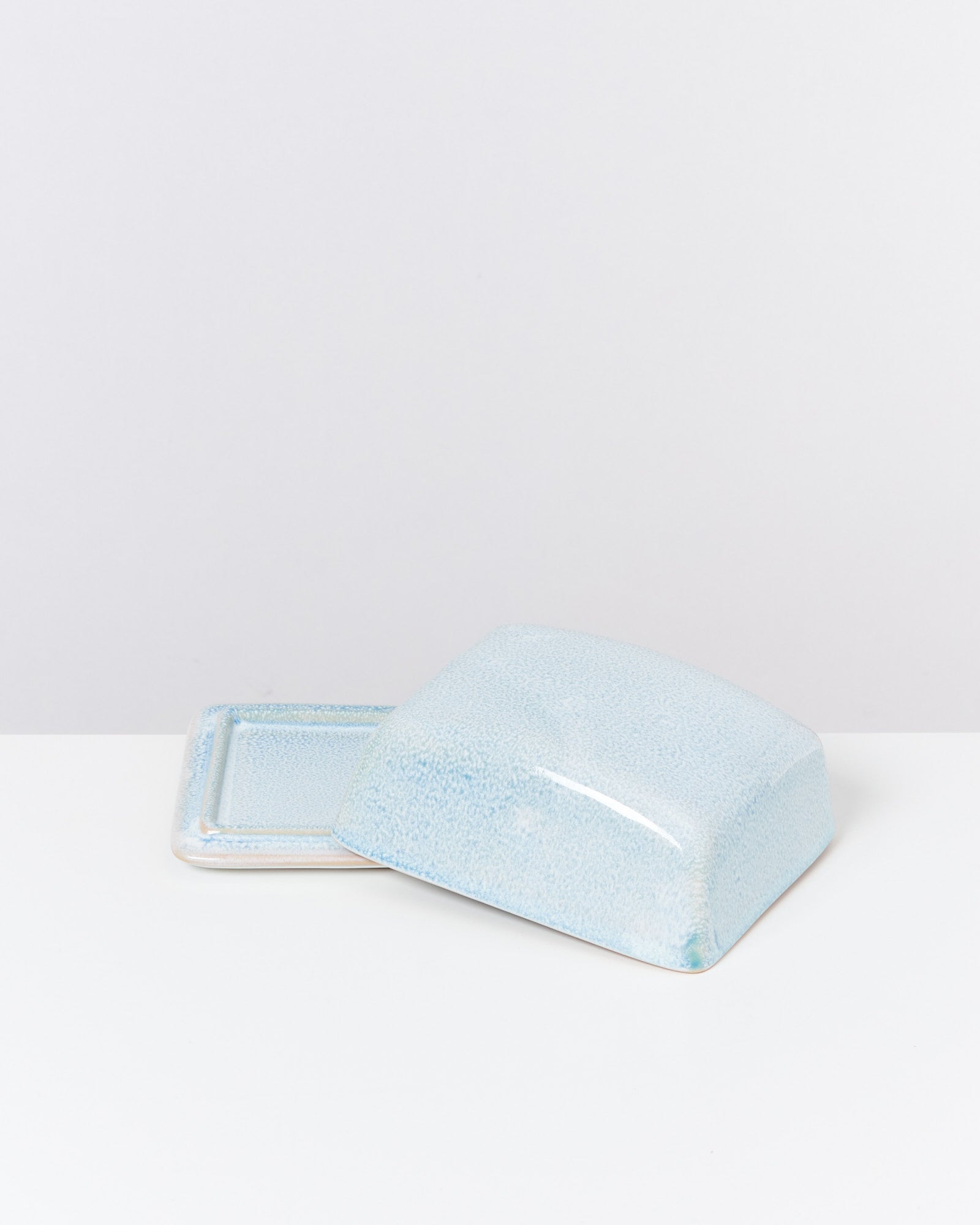 Hellblaue Keramik-Butterdose mit einem abgenommenen Deckel auf weißem Hintergrund.