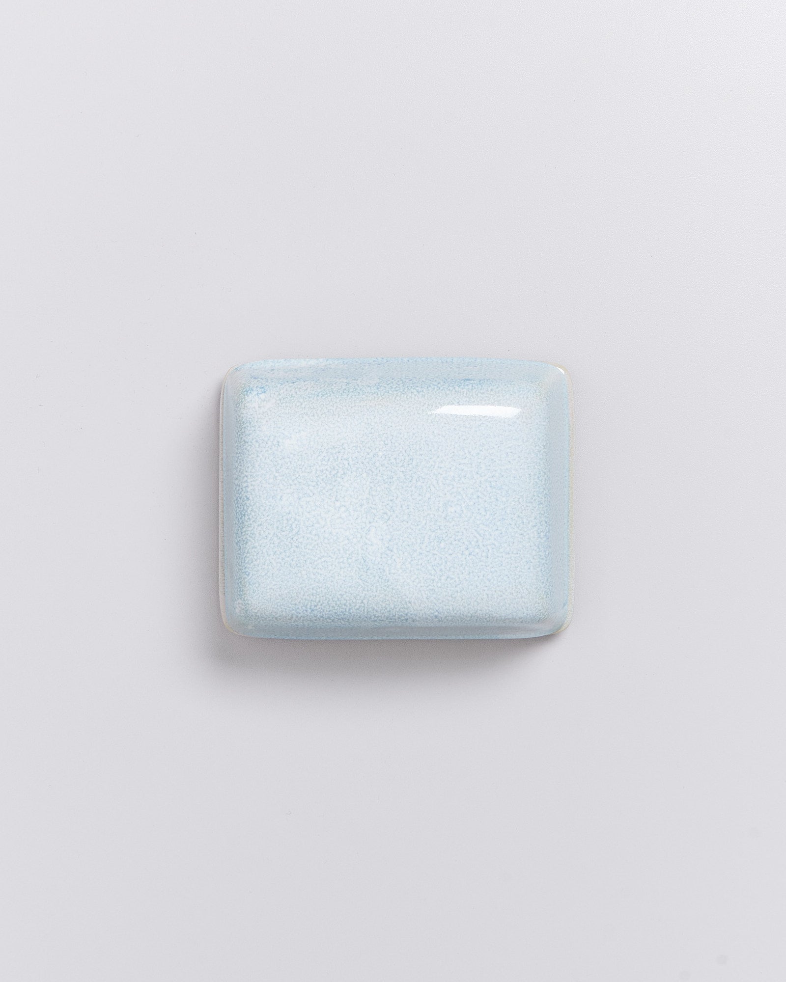 Ein glänzend blaues, quadratisches Seifenstück liegt auf einem weißen Hintergrund.