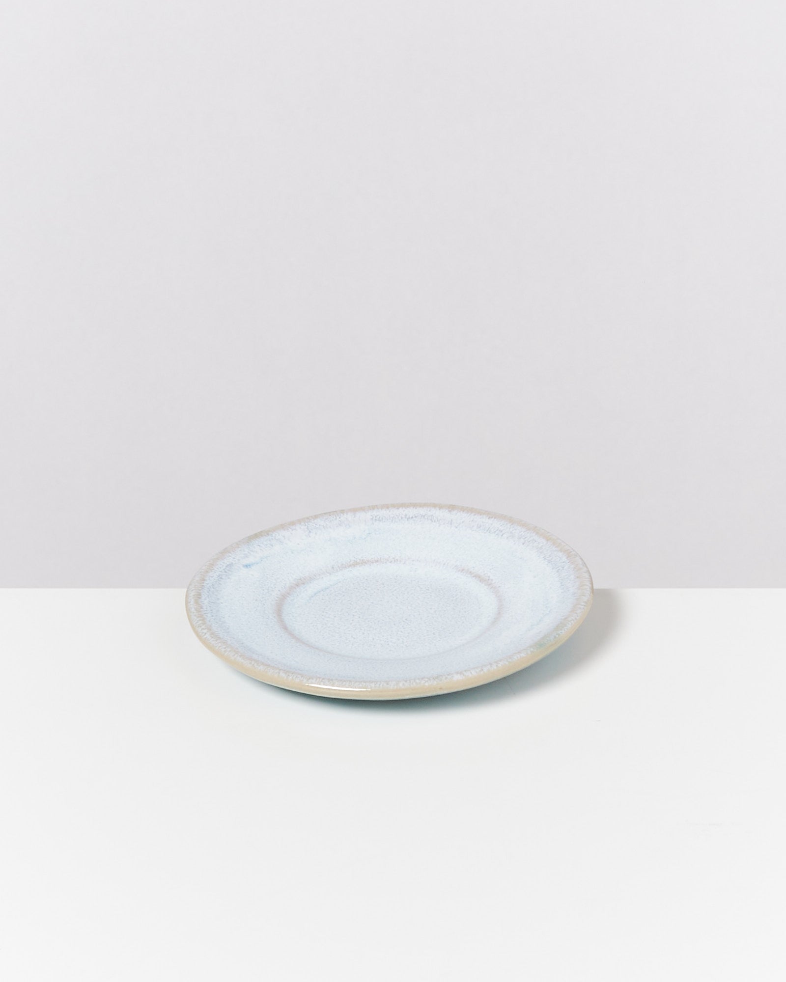 Ein hellblauer Keramikteller steht auf einer weißen Oberfläche vor einem neutralen Hintergrund.
