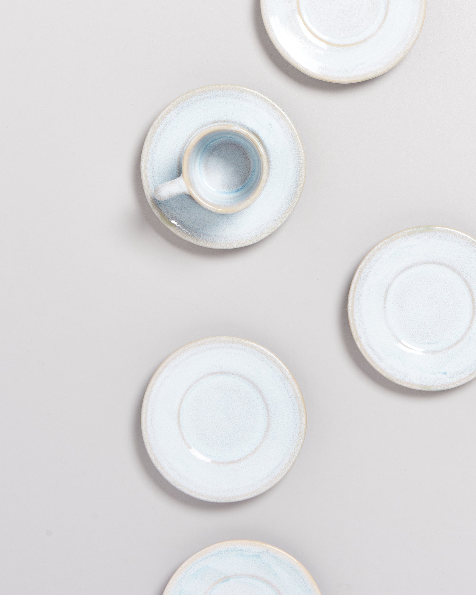 Fünf hellblaue Untertassen und eine passende Tasse auf einem hellgrauen Hintergrund arrangiert.