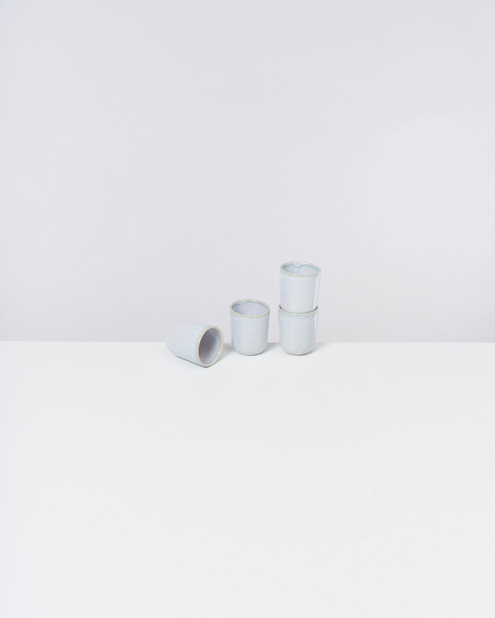 Vier gestapelte, hellblaue Keramikbecher auf einem weißen Tisch vor einem grauen Hintergrund.