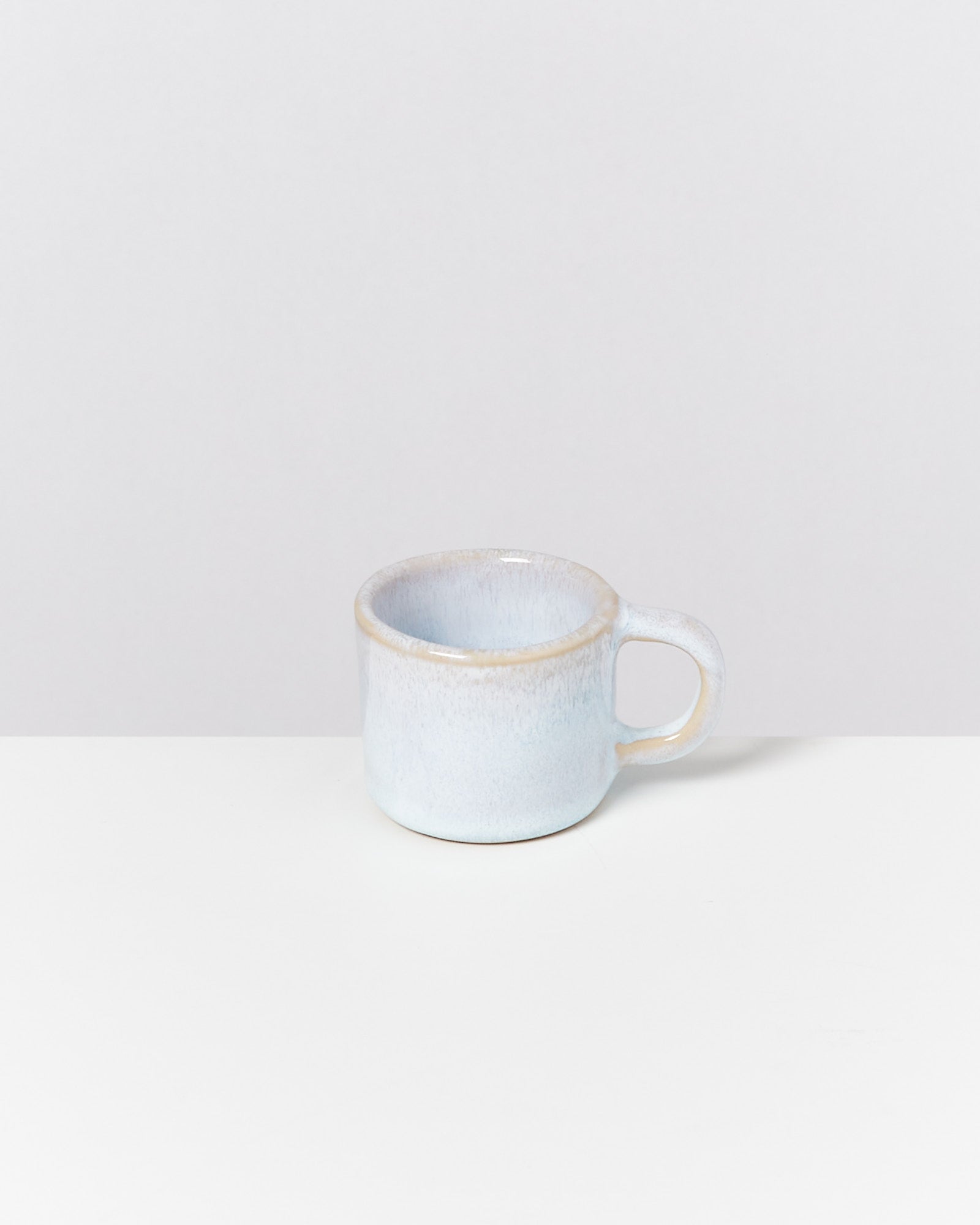 Ein kleiner, hellblauer Keramikbecher steht auf einem weißen Tisch vor einem grauen Hintergrund.