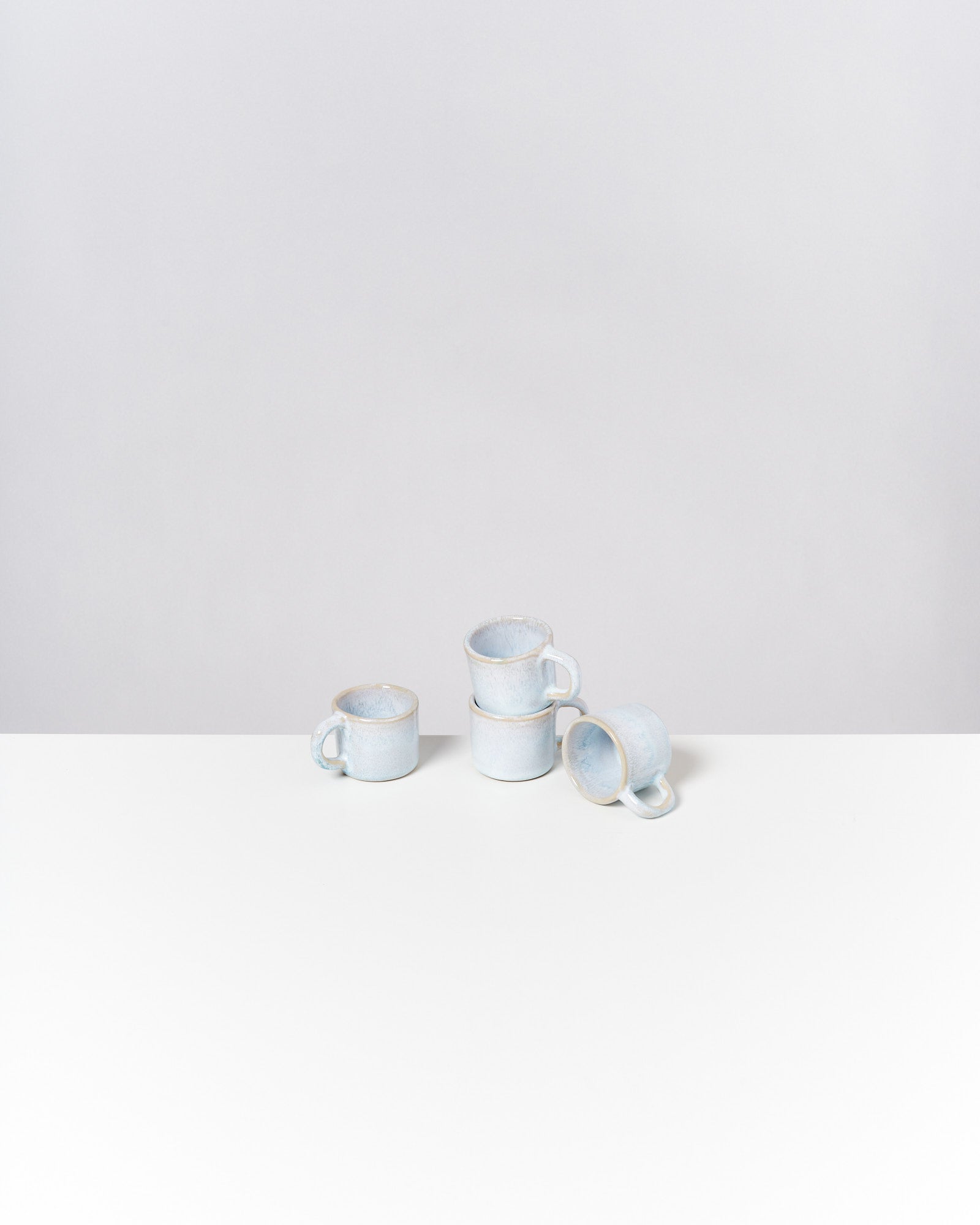 Drei gestapelte blaue Tassen und eine umgedrehte Tasse auf weißem Tisch vor grauem Hintergrund.