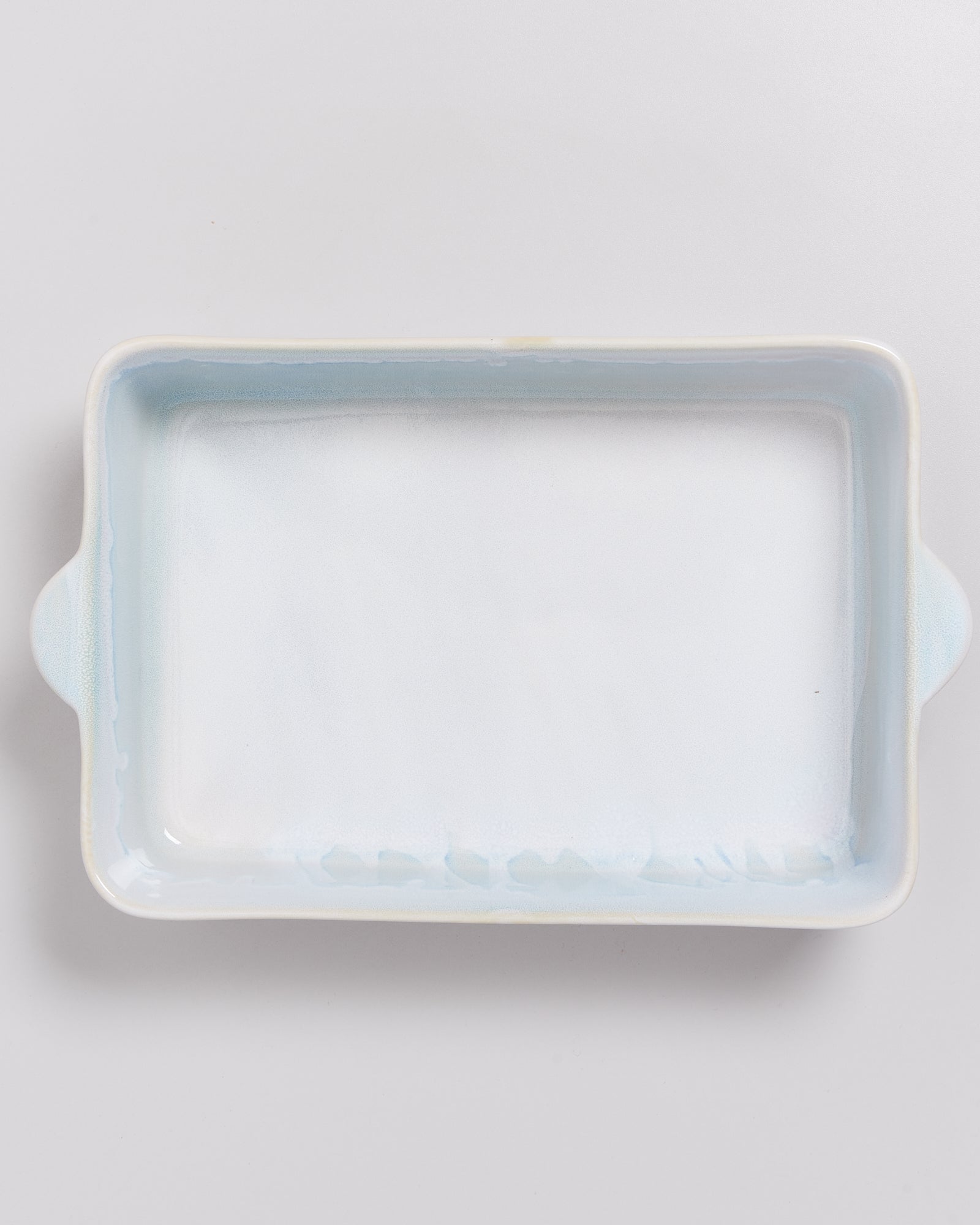 Weiße rechteckige Backform mit Griffen auf einem hellen Hintergrund.