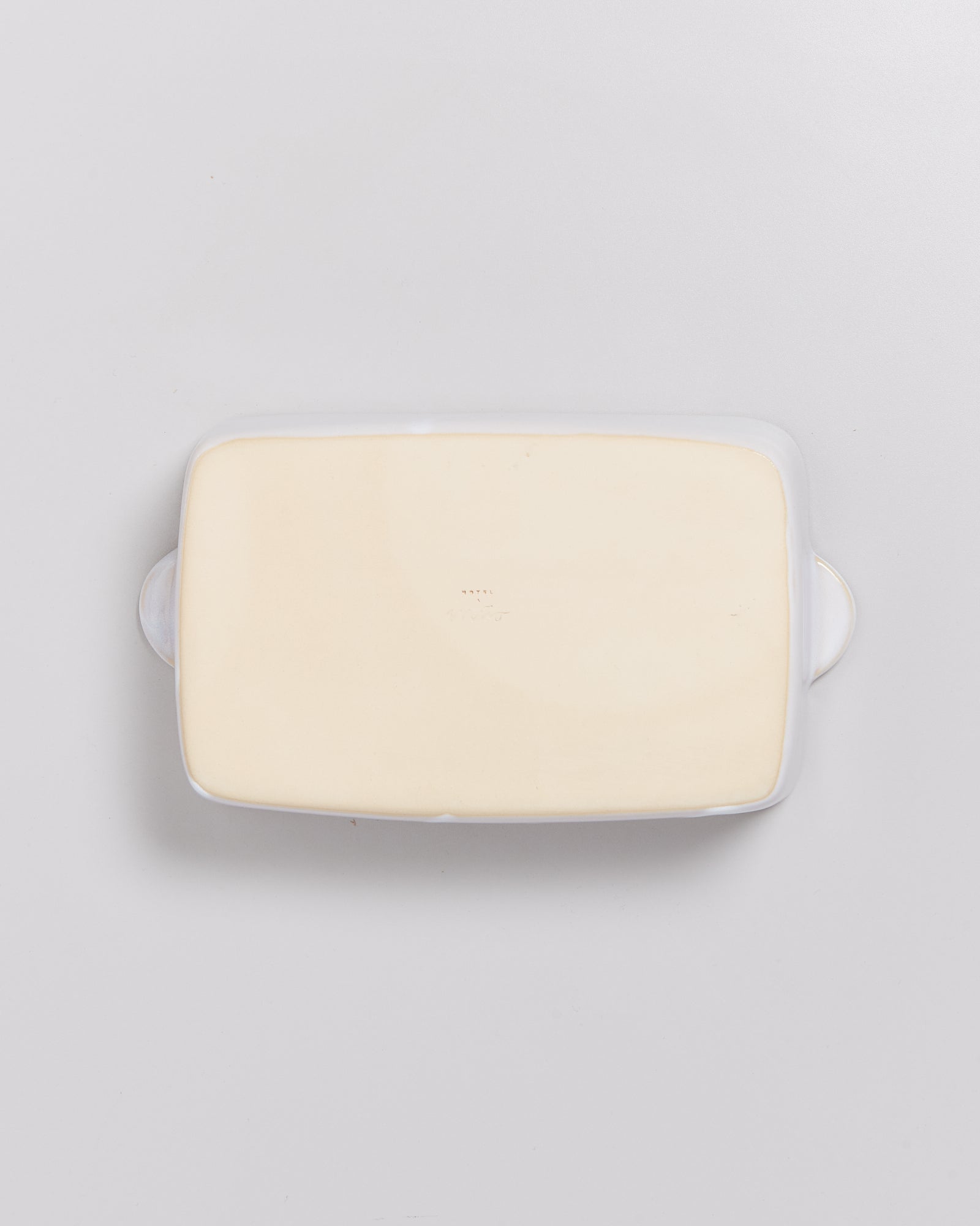 Rechteckige Auflaufform in Weiß mit Griffen auf einer grauen Oberfläche.