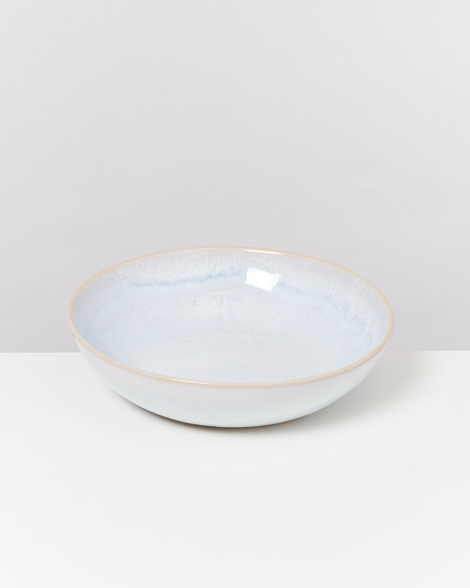 Große, flache, hellblaue Keramikschüssel auf einer weißen Oberfläche vor einem grauen Hintergrund.
