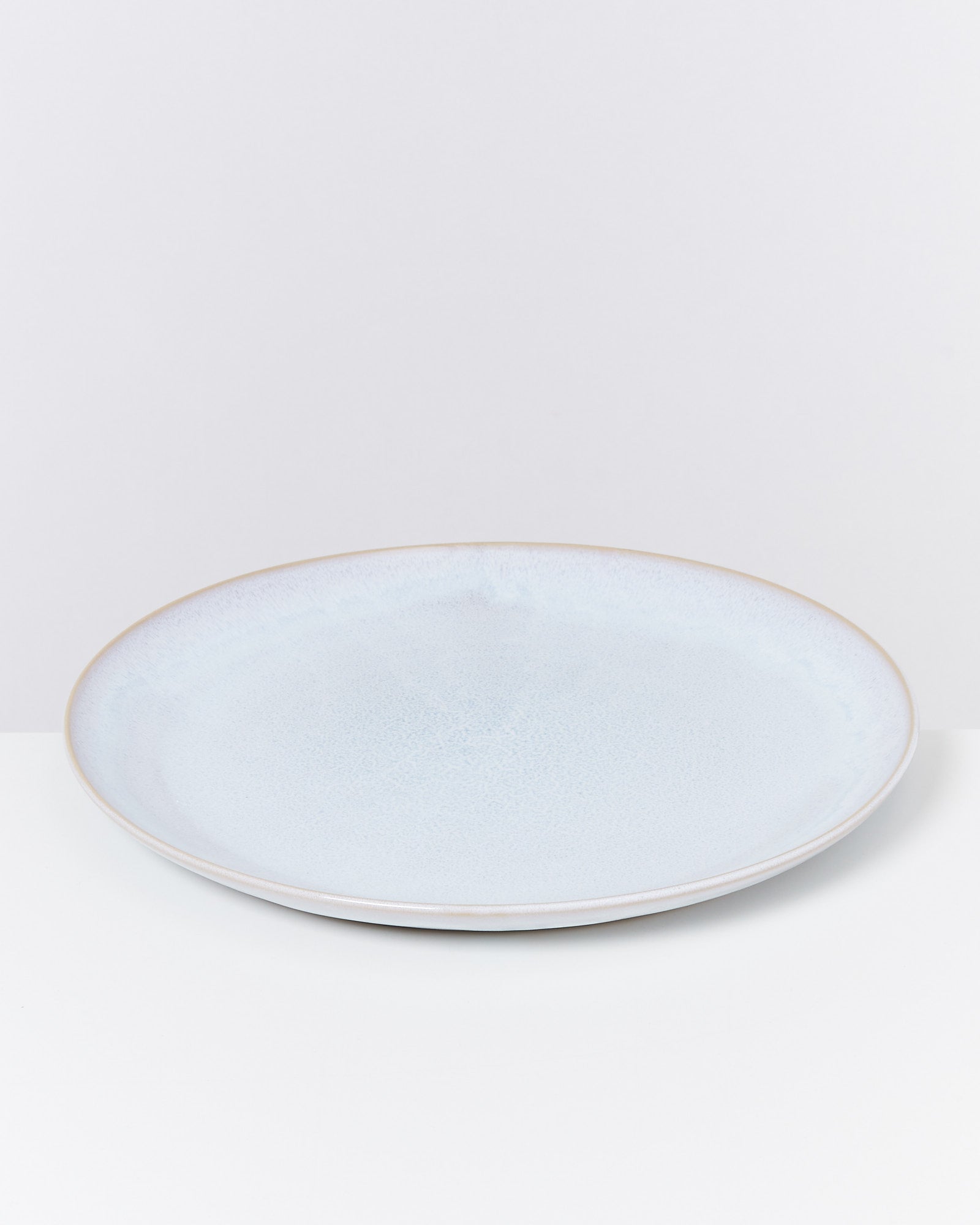 Ein weißer, flacher Porzellanteller auf einem weißen Hintergrund.