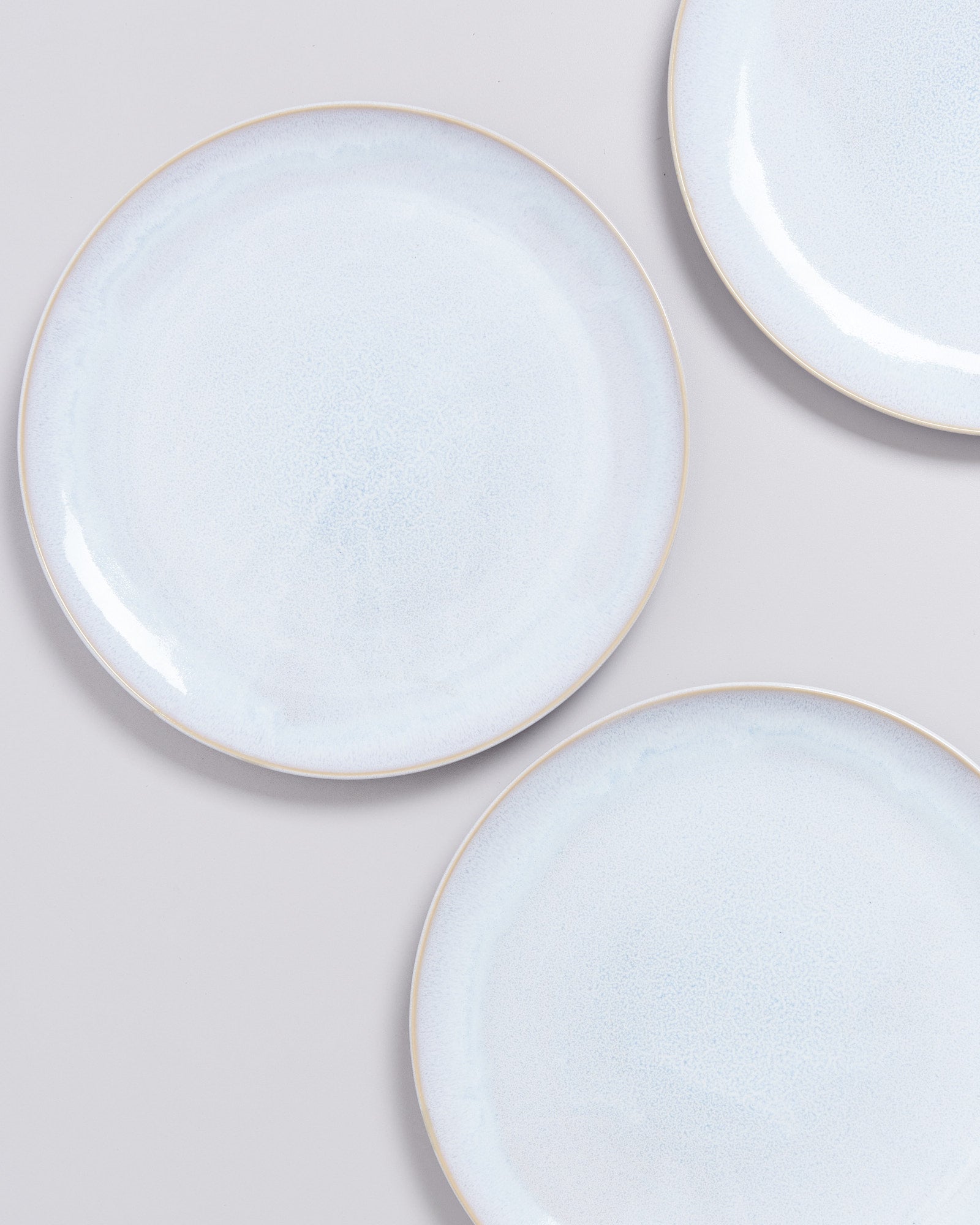 Drei weiße, runde Teller liegen auf einer hellgrauen Oberfläche.