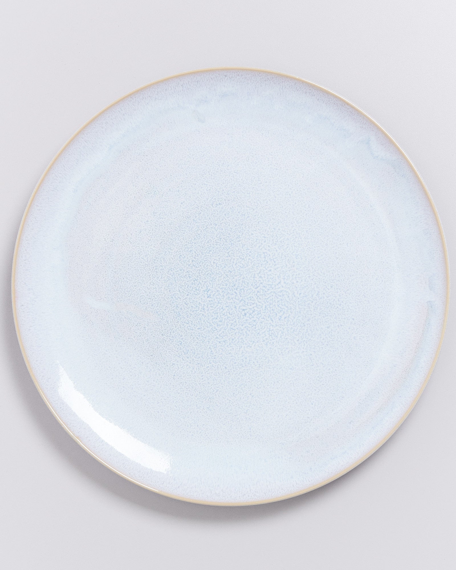 Ein runder, hellblauer Keramikteller mit glattem, glänzendem Finish auf einem neutralen Hintergrund.