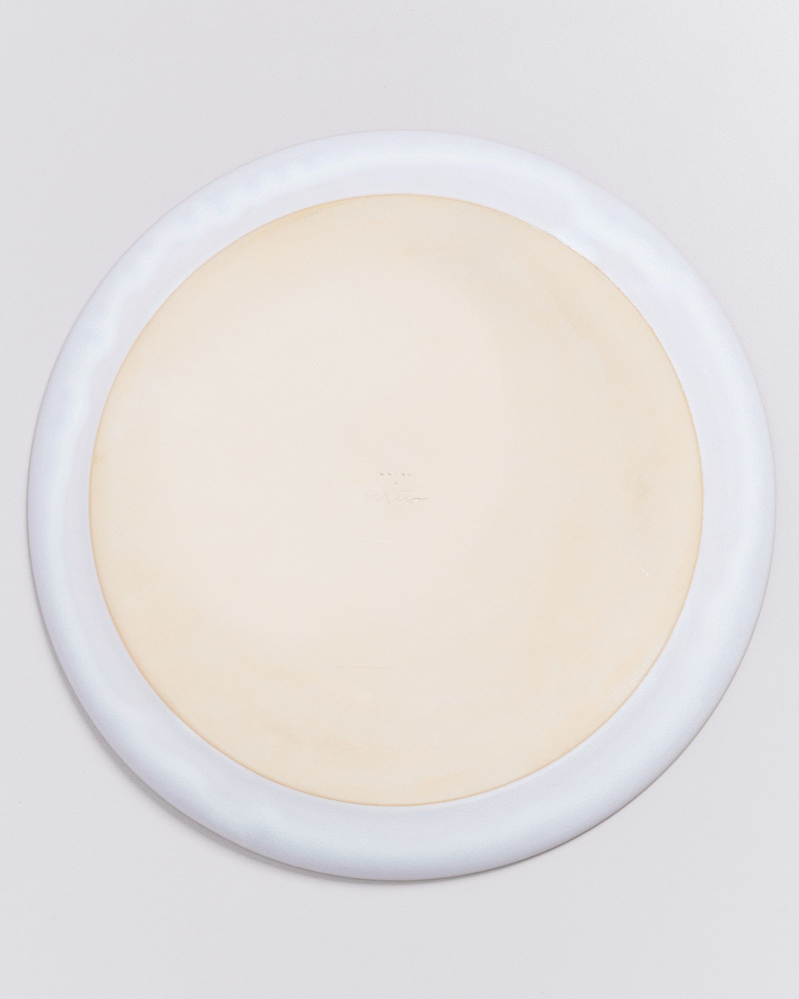 Beigefarbener, runder Teller mit einem schmalen, weißen Rand auf weißem Hintergrund.