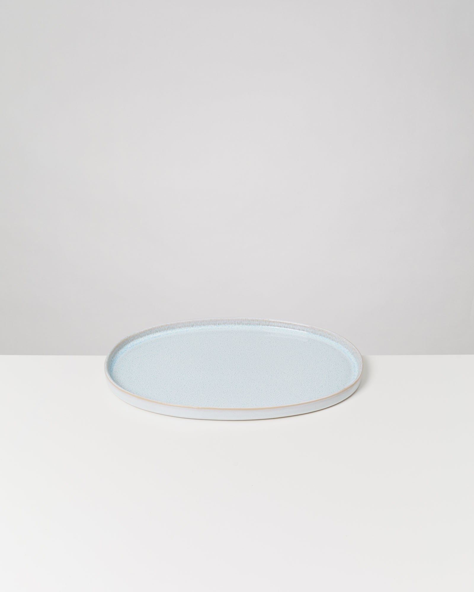 Runder, flacher, hellblauer Teller auf einem weißen Tisch vor neutralem Hintergrund.