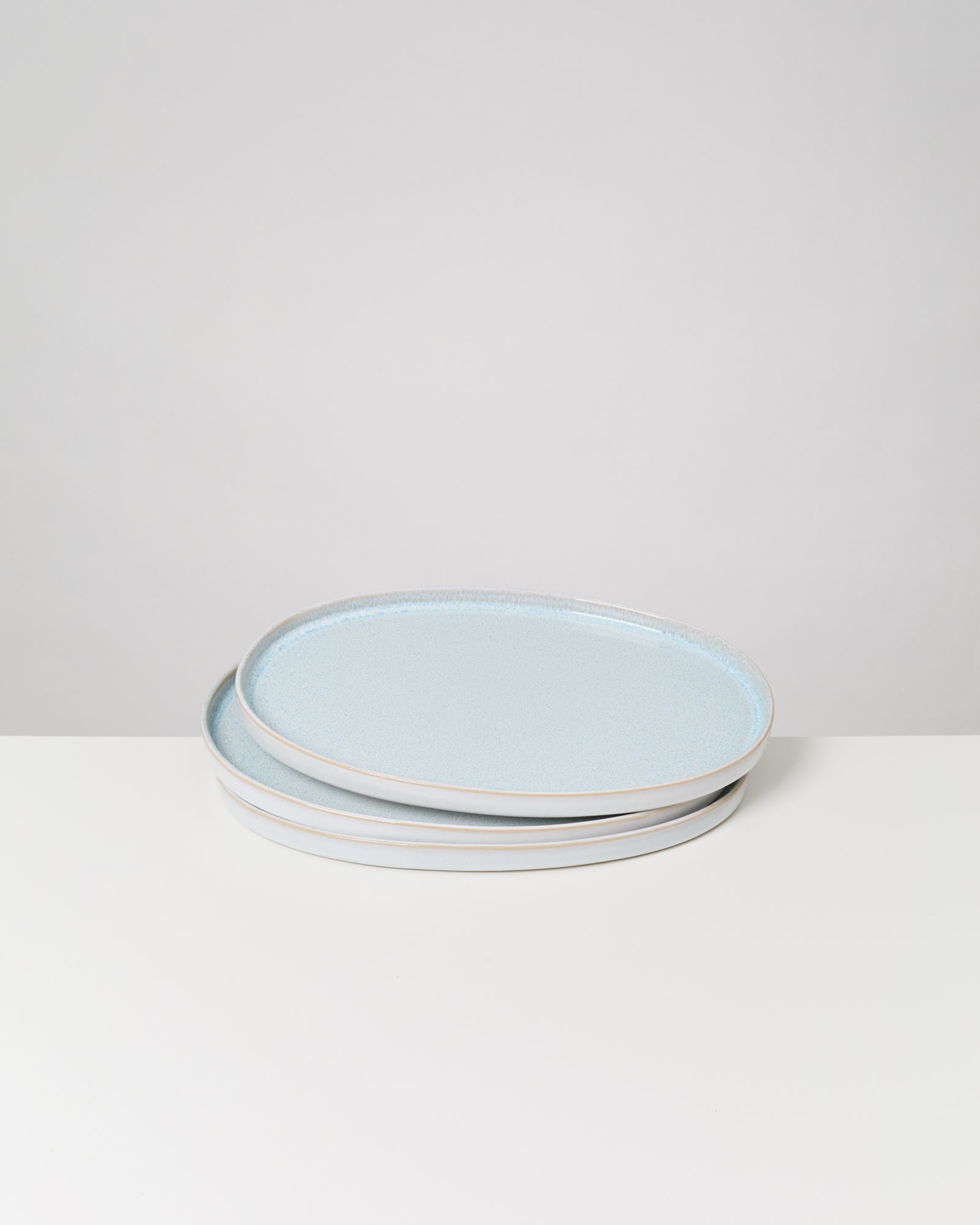 Stapel ovaler, hellblauer Keramikteller auf weißem Tisch, minimalistisch dargestellt.