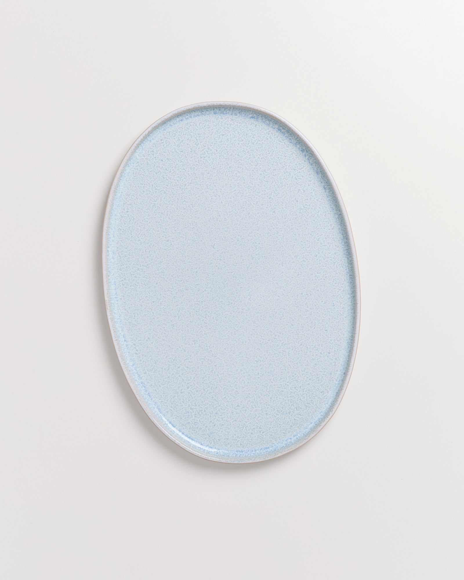 Hellblauer ovaler Teller mit feiner Körnung auf einem weißen Hintergrund.