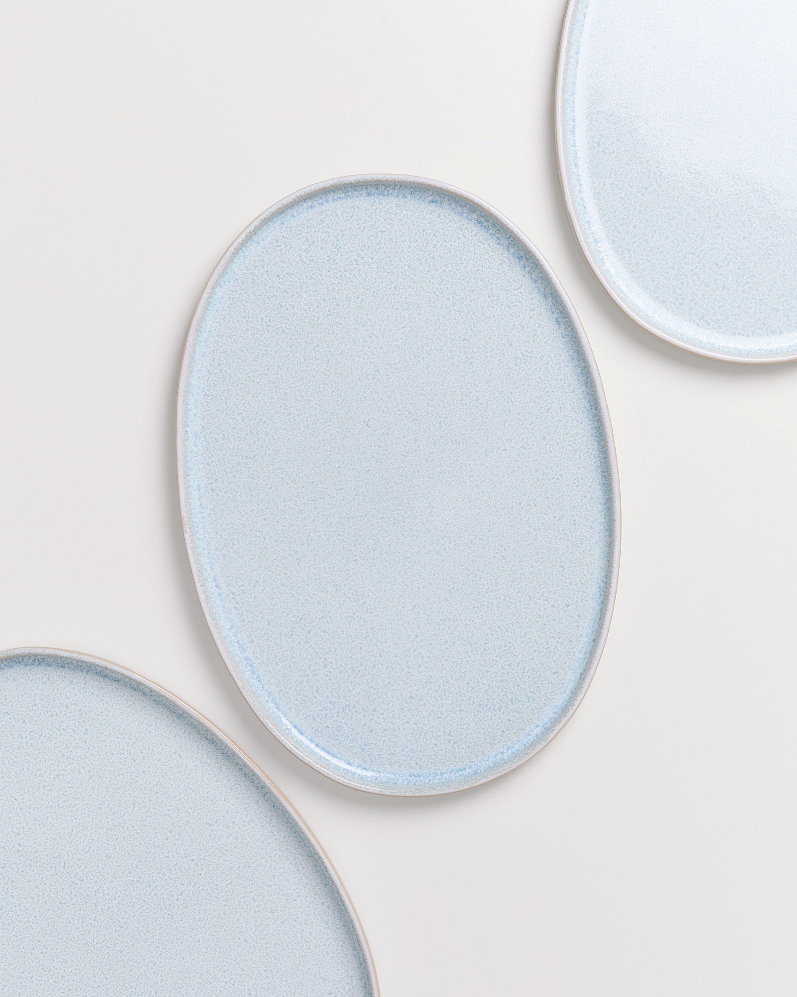 Drei ovale, hellblaue Teller liegen auf einer weißen Oberfläche, jeweils zu Teilen sichtbar.