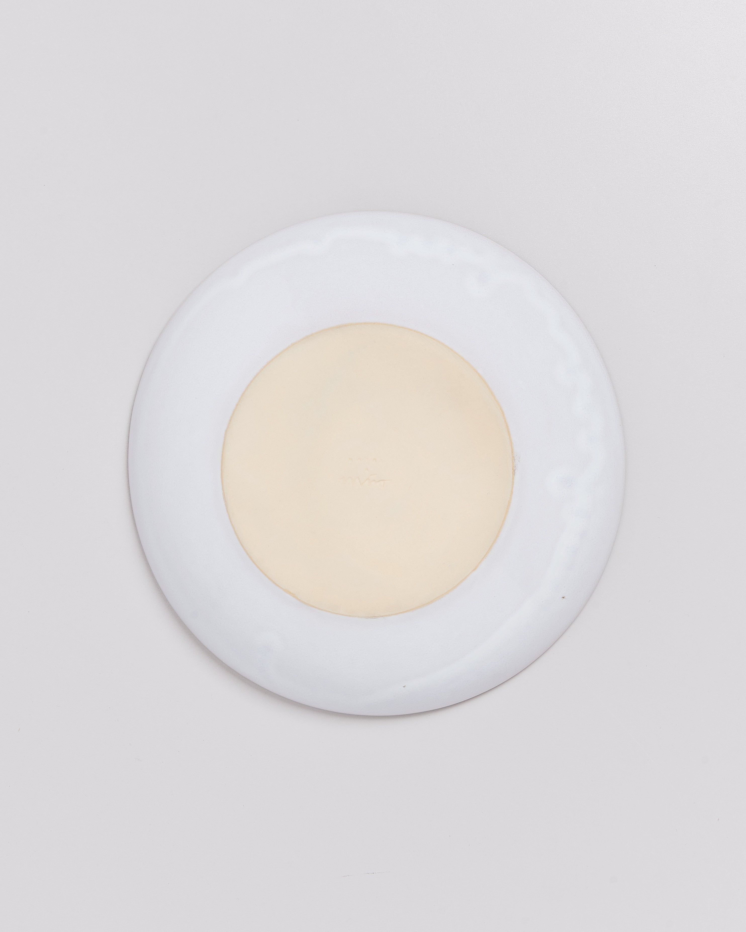 Runde, flache, zweifarbige Schale mit cremefarbenem Zentrum und weißem Rand auf grauem Hintergrund.