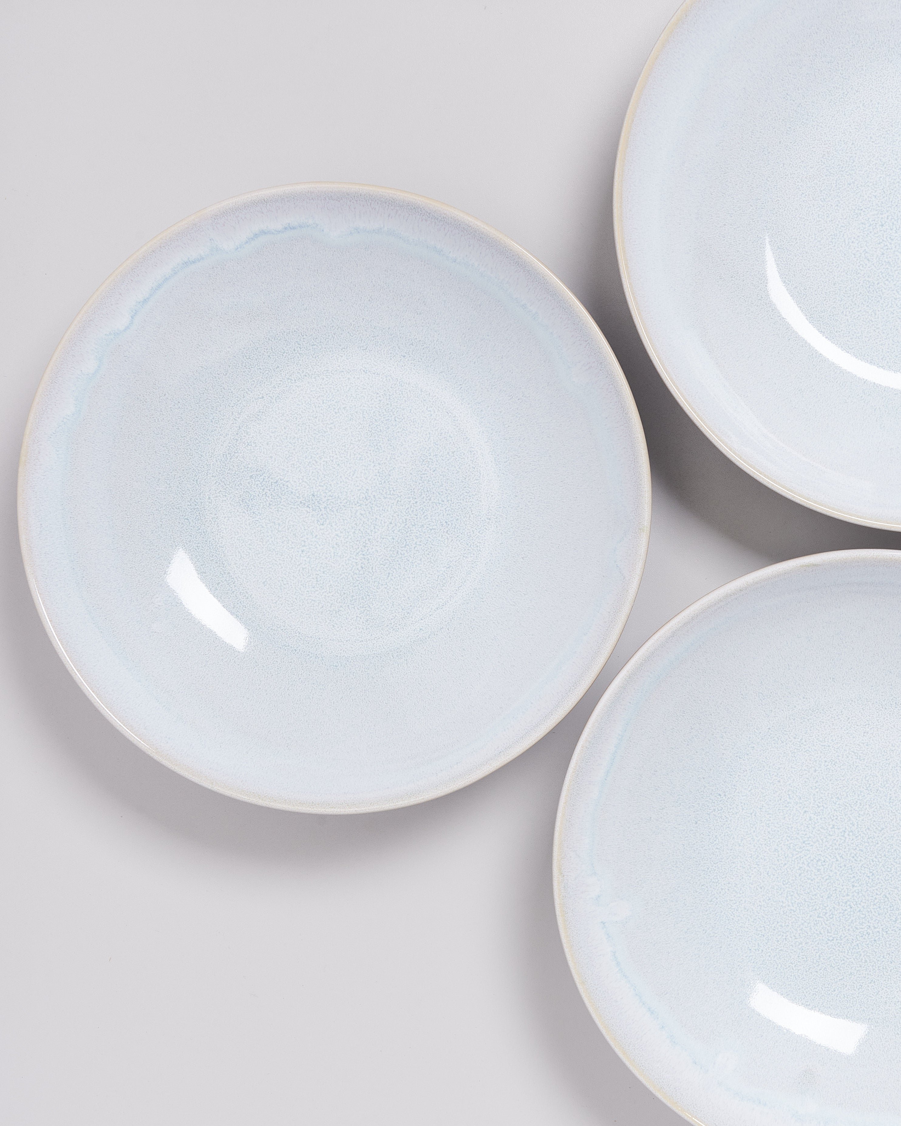 Drei helle, runde Keramikteller auf einer grauen Oberfläche arrangiert.