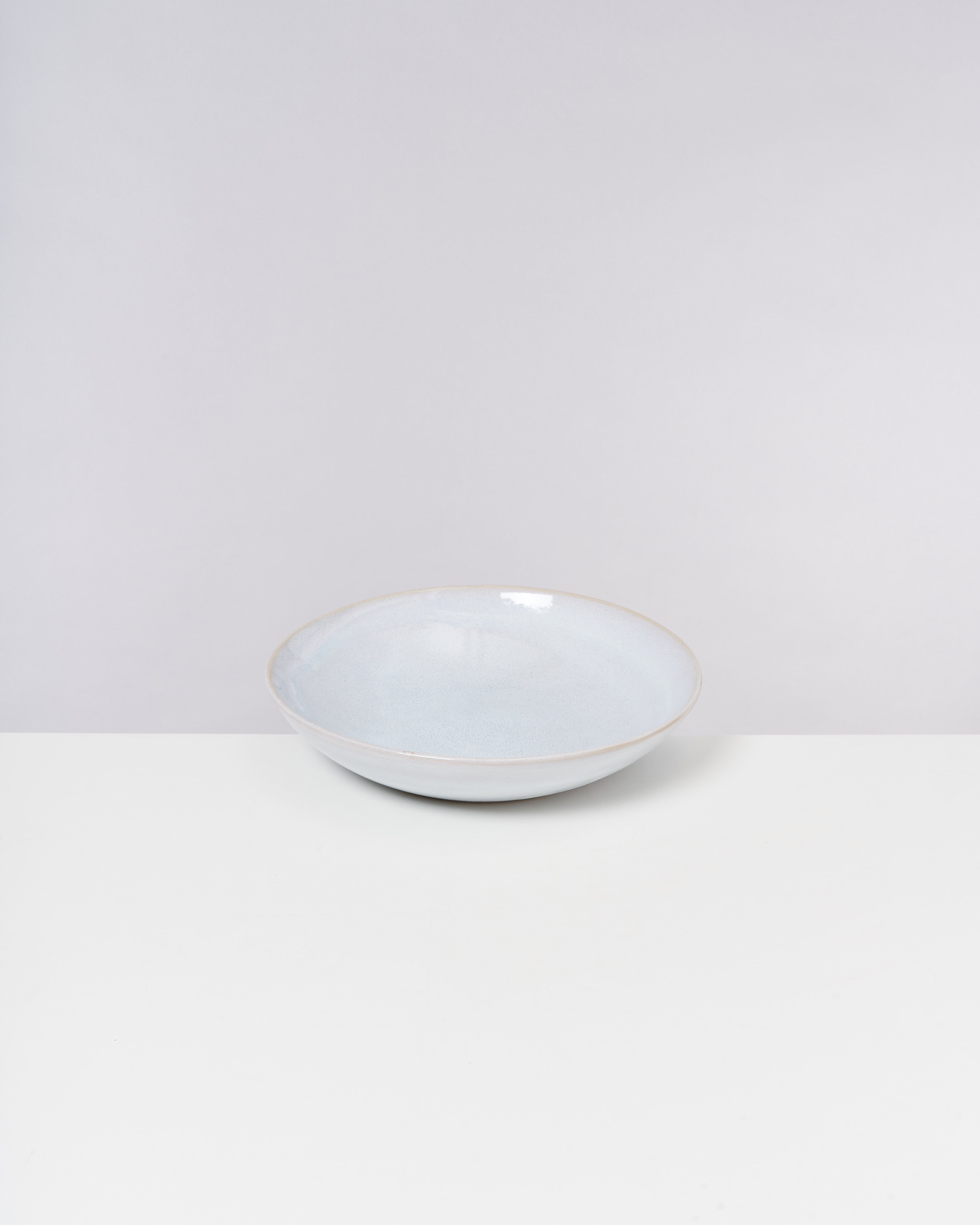 Flacher heller Keramikteller auf einem weißen Hintergrund.