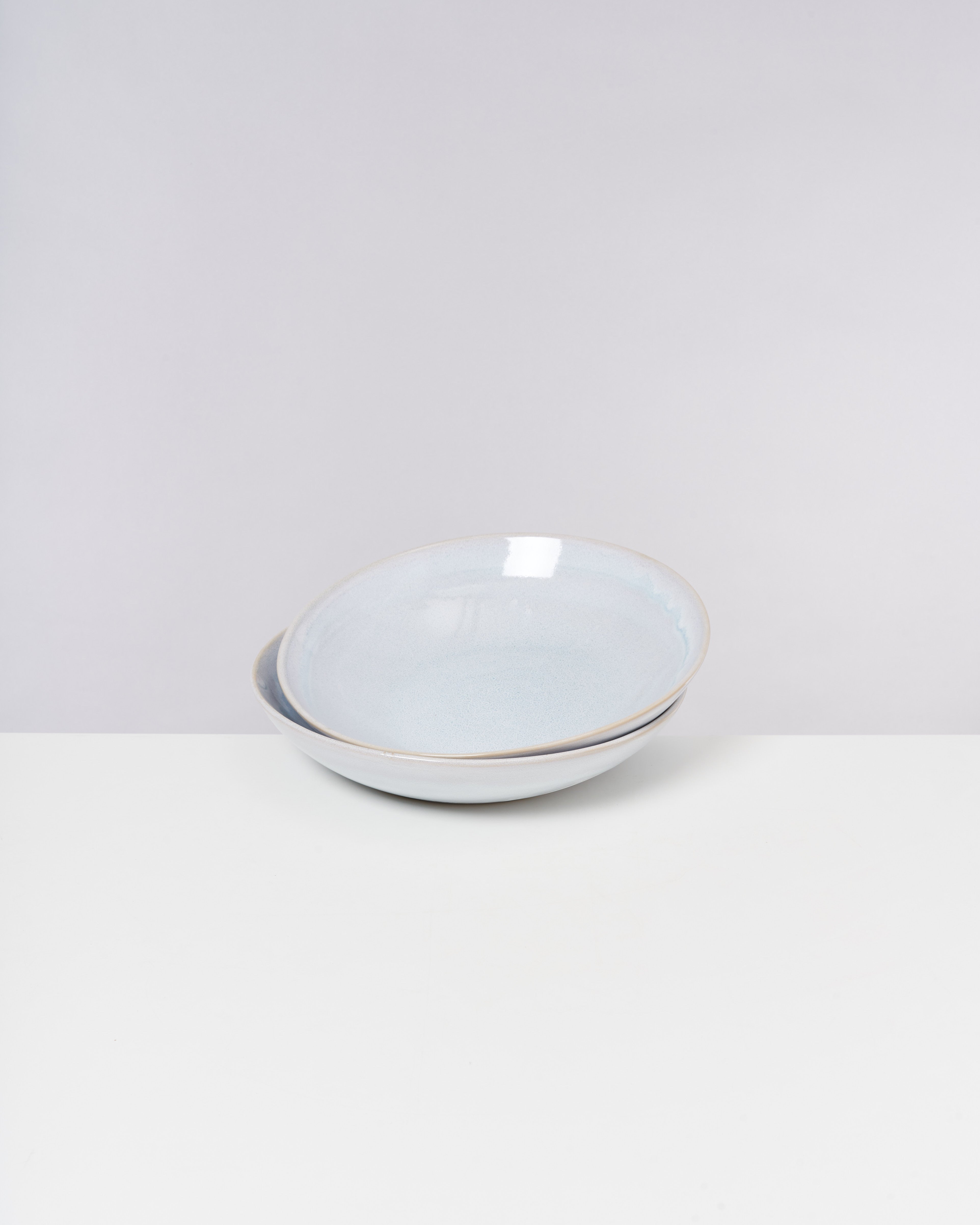 Zwei übereinander gestapelte, hellblaue Keramikschalen mit dezentem Glanz auf einem weißen Hintergrund.