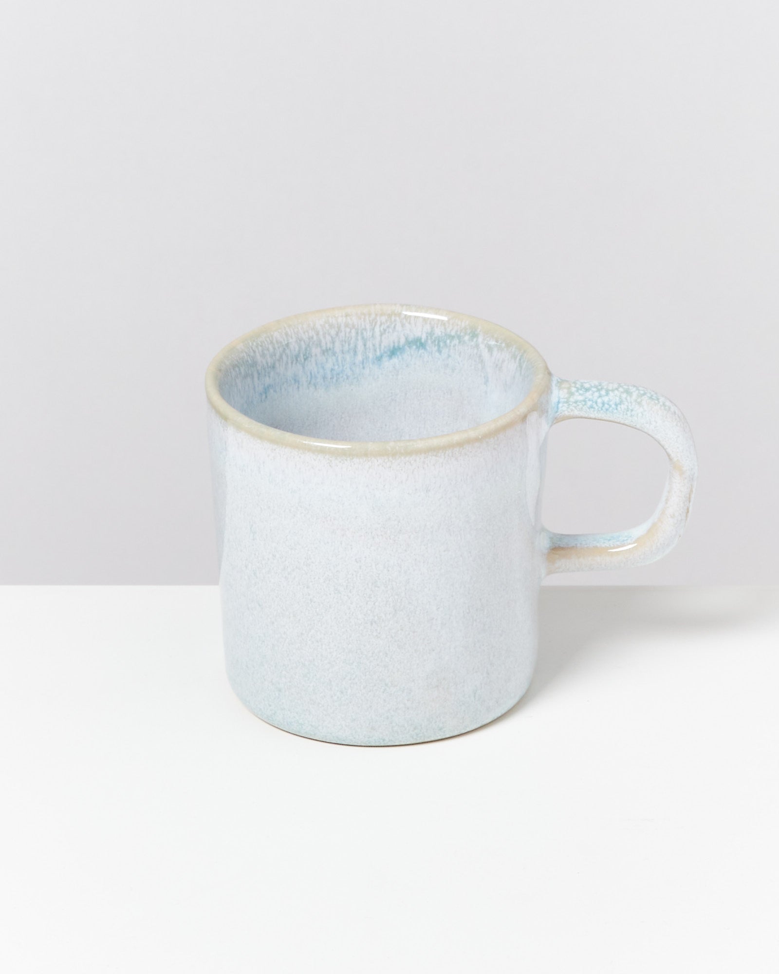 Hellblaue Keramiktasse mit leichtem Farbverlauf auf einer weißen Oberfläche vor grauem Hintergrund.