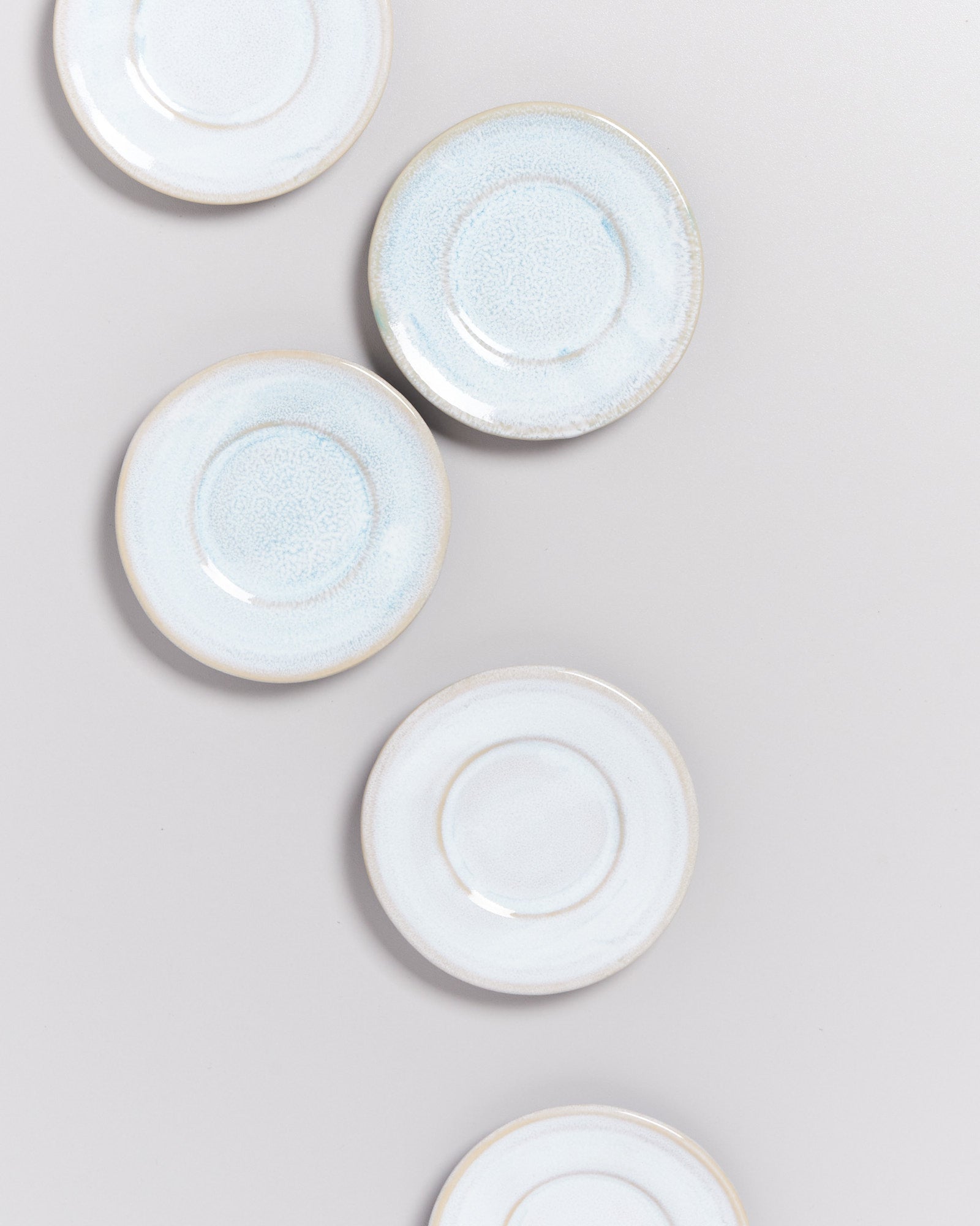 Fünf kleine, runde, blassblaue Teller liegen verstreut auf einer hellgrauen Oberfläche.