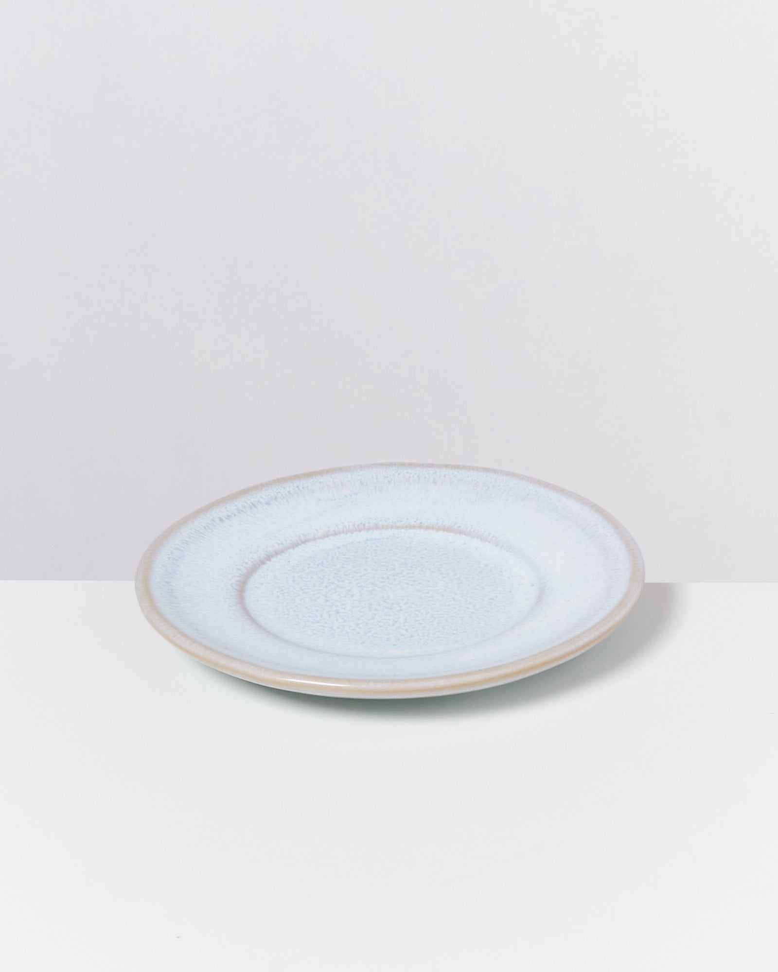 Hellblauer Keramikteller auf weißer Oberfläche vor grauem Hintergrund.