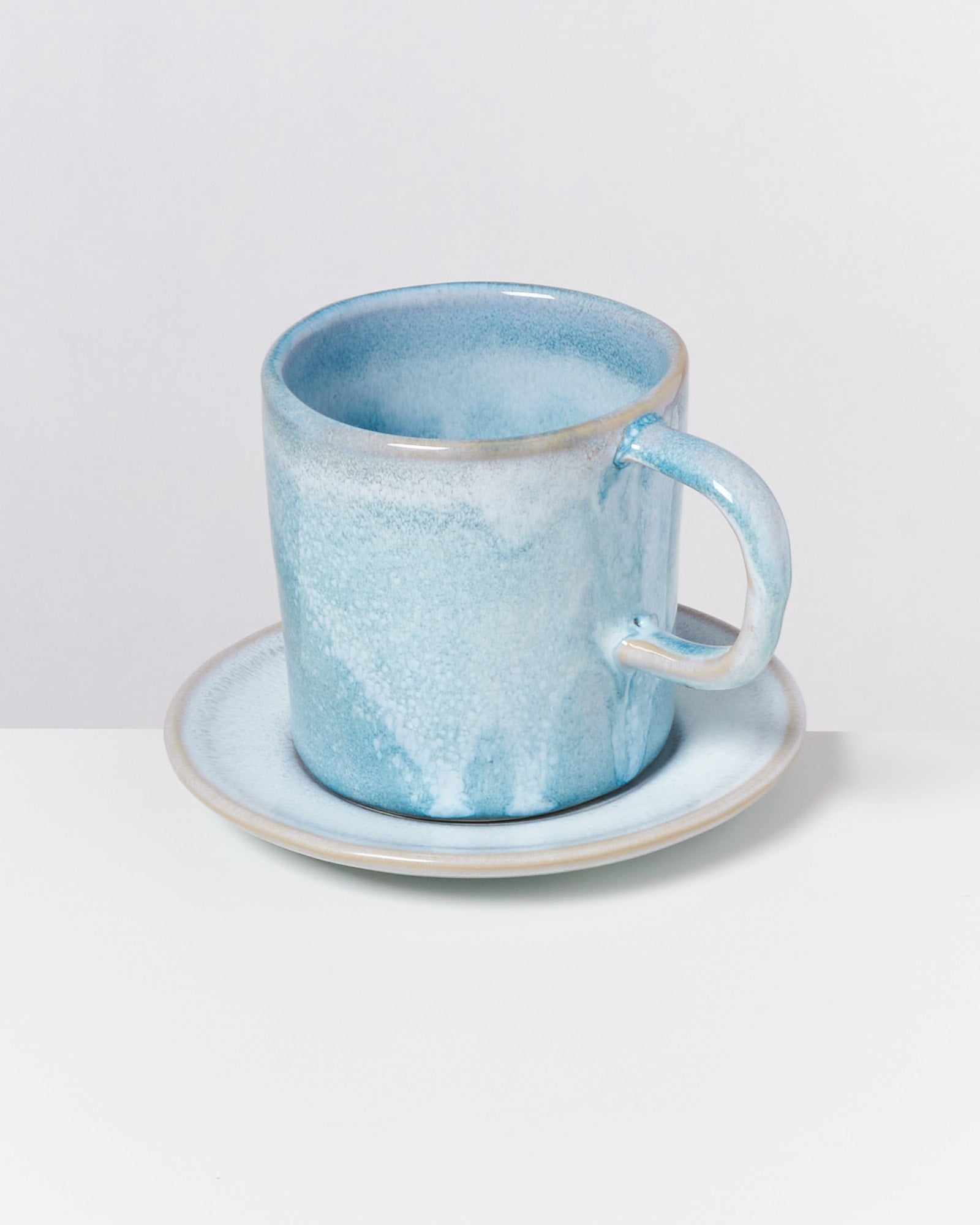 Blaue Keramiktasse mit passender Untertasse auf weißem Hintergrund.