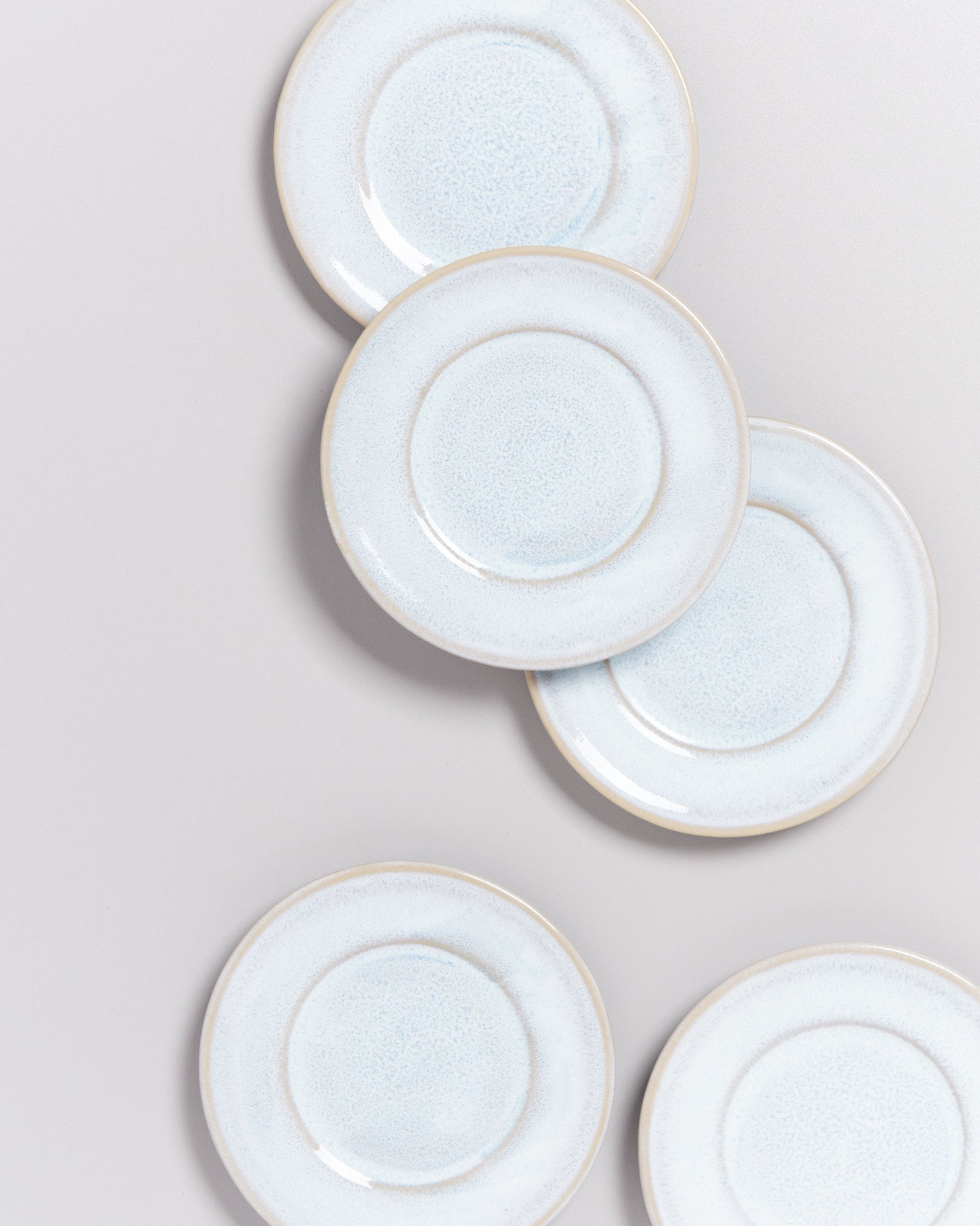 Fünf helle, runde Teller mit leichtem Blaustich liegen auf einer hellen Oberfläche.