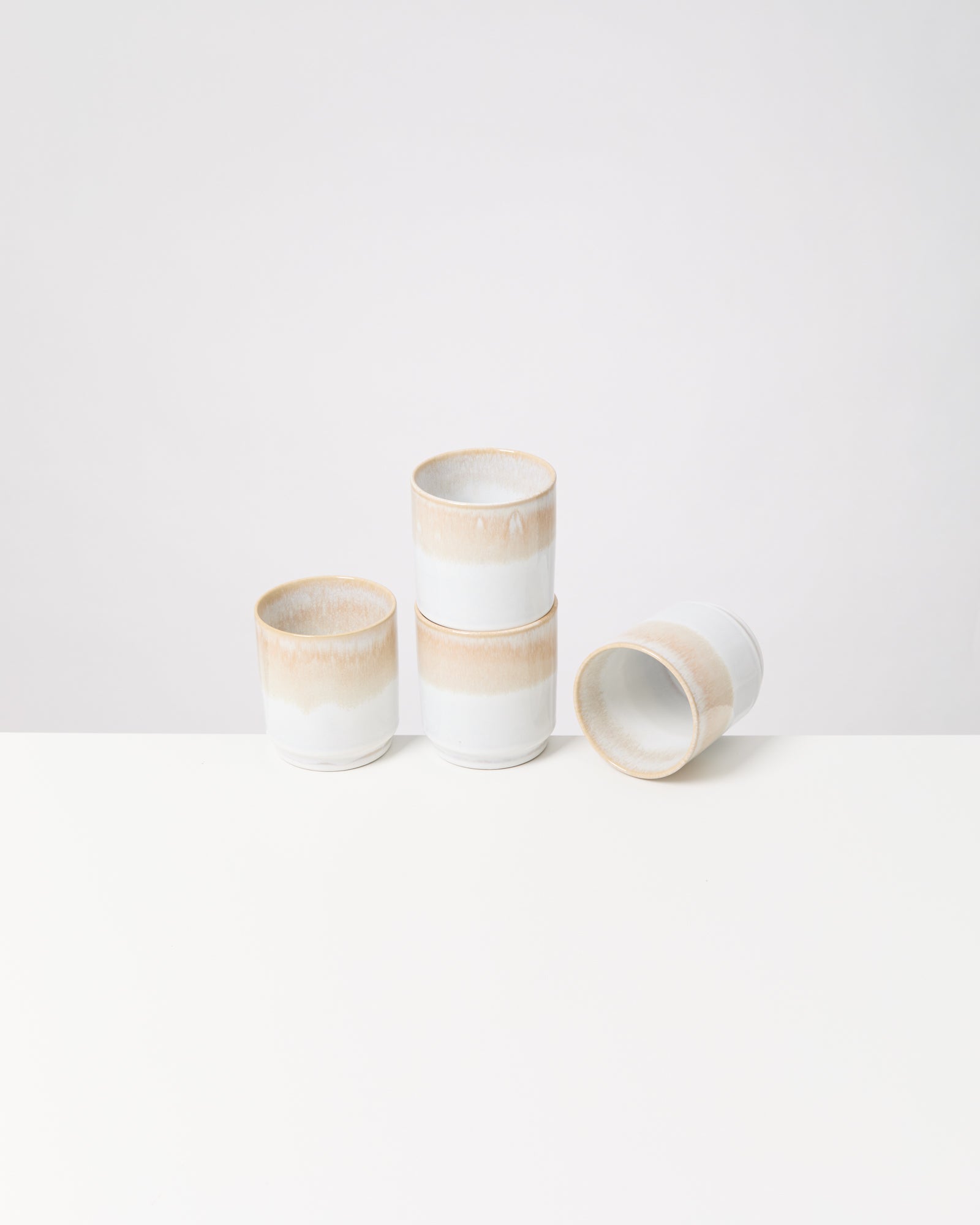 Vier stapelbare, beige-weiße Keramiktassen vor einem weißen Hintergrund.