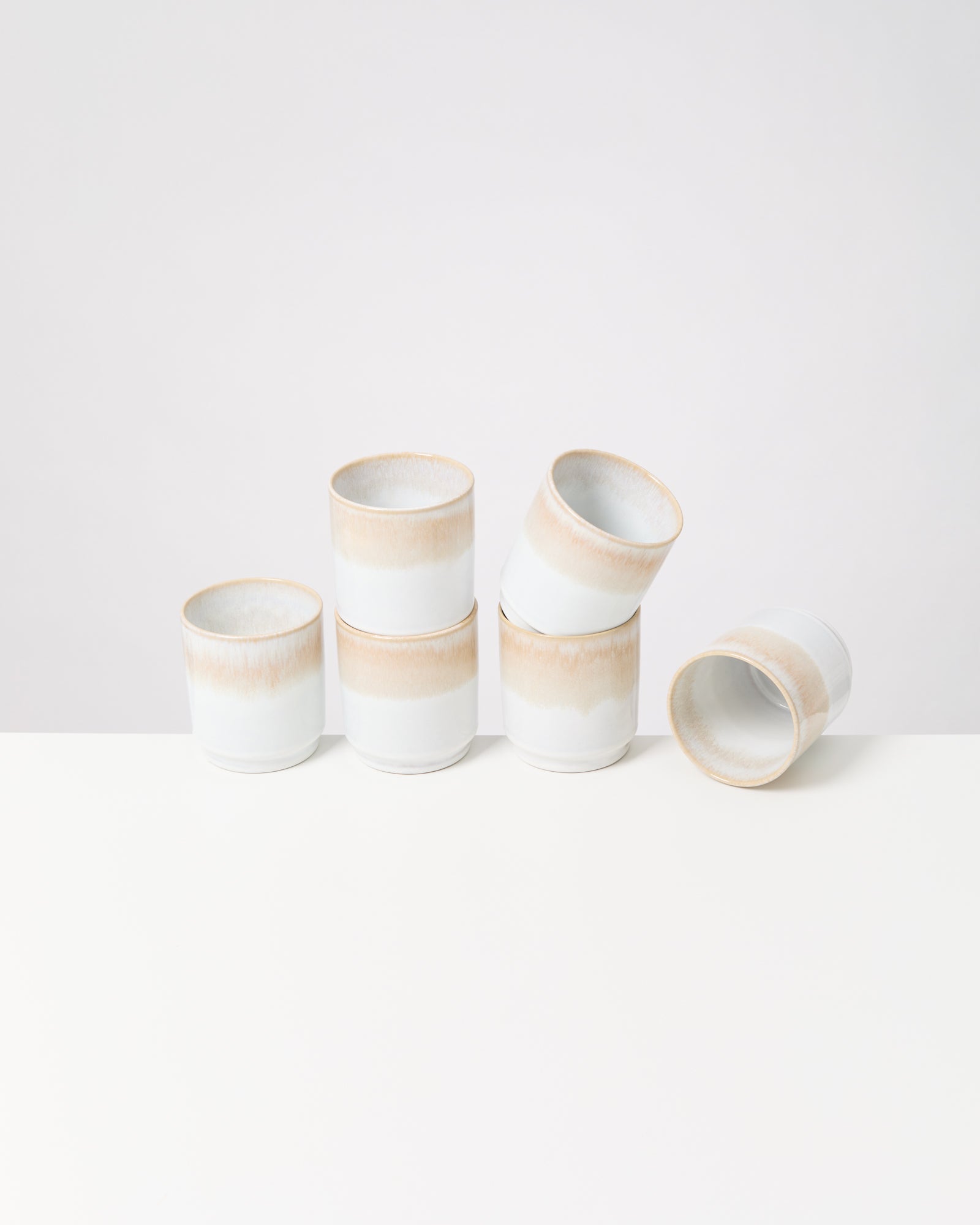Sechs gestapelte, weiße Keramiktassen mit beige Schattierungen auf einem weißen Hintergrund.