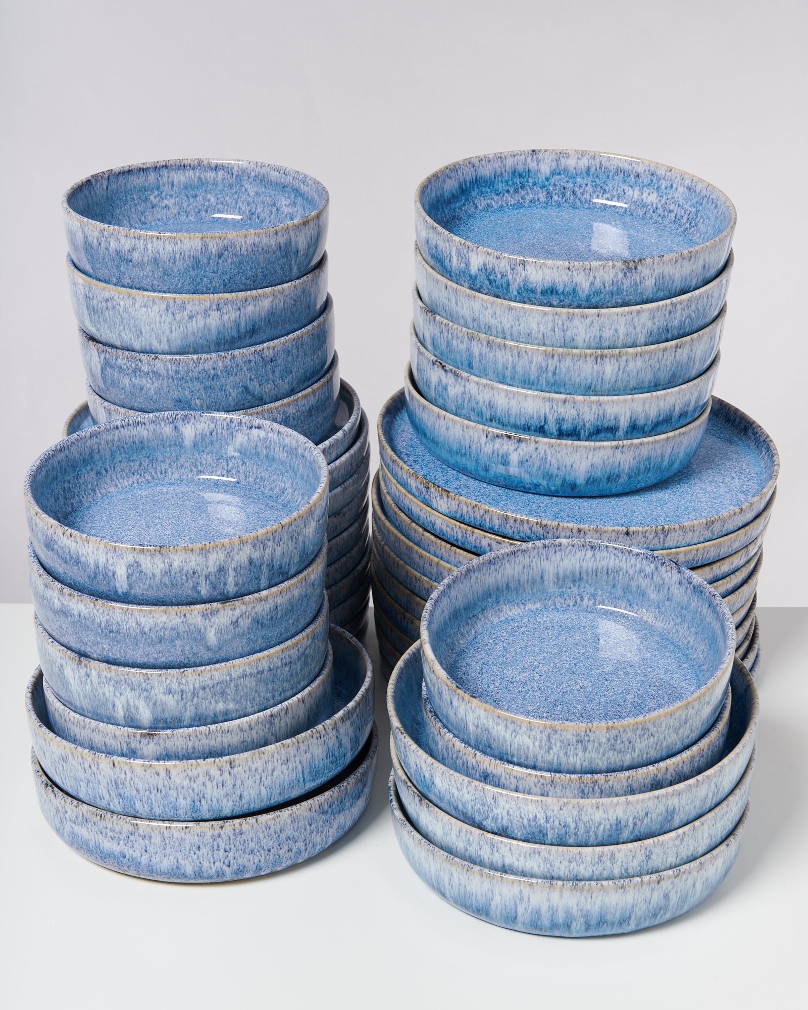 Mehrere Stapel blauer Keramikteller in unterschiedlichen Höhen auf einem weißen Untergrund.