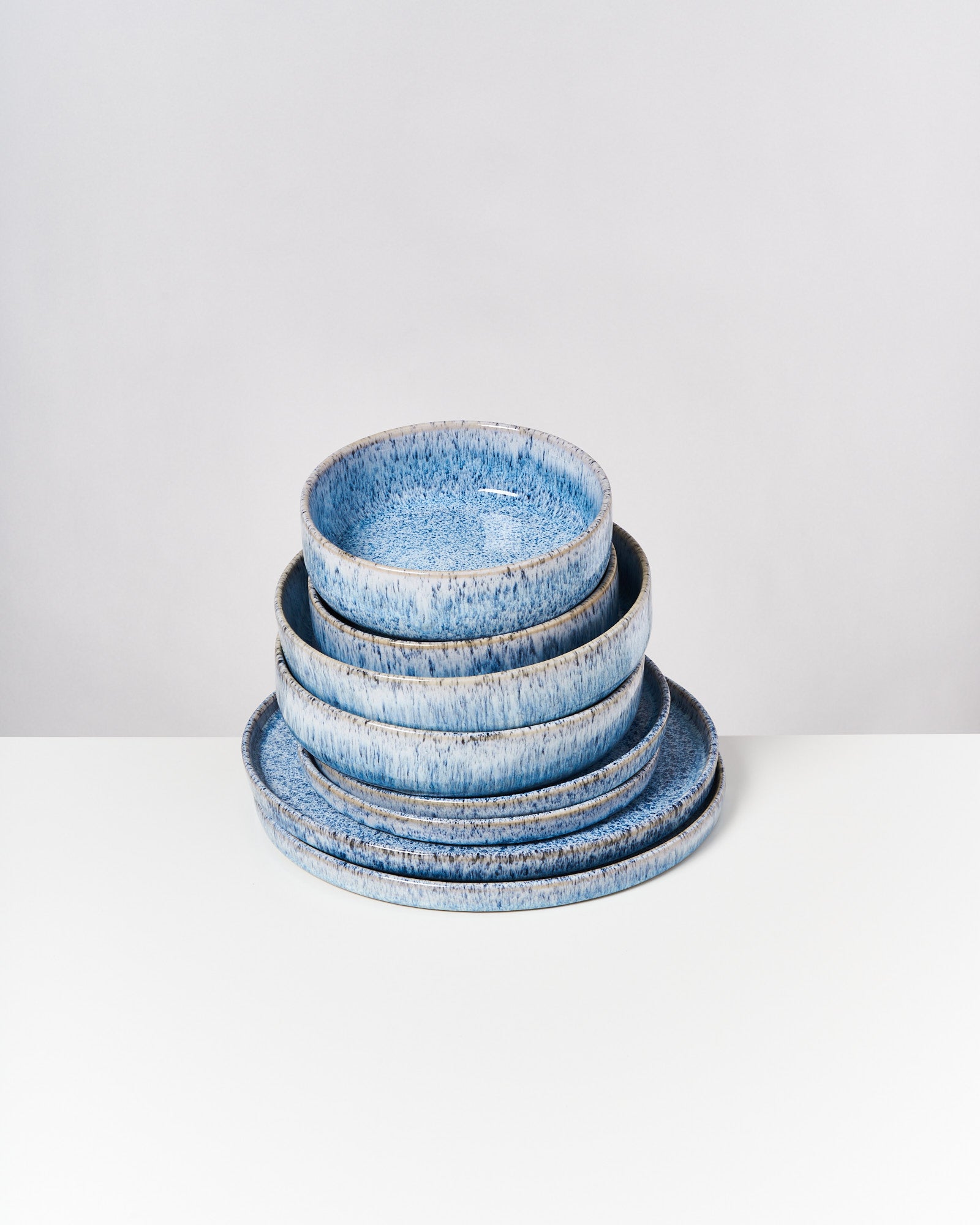 Ein Stapel blauer, gesprenkelter Teller und Schüsseln auf einer weißen Oberfläche.