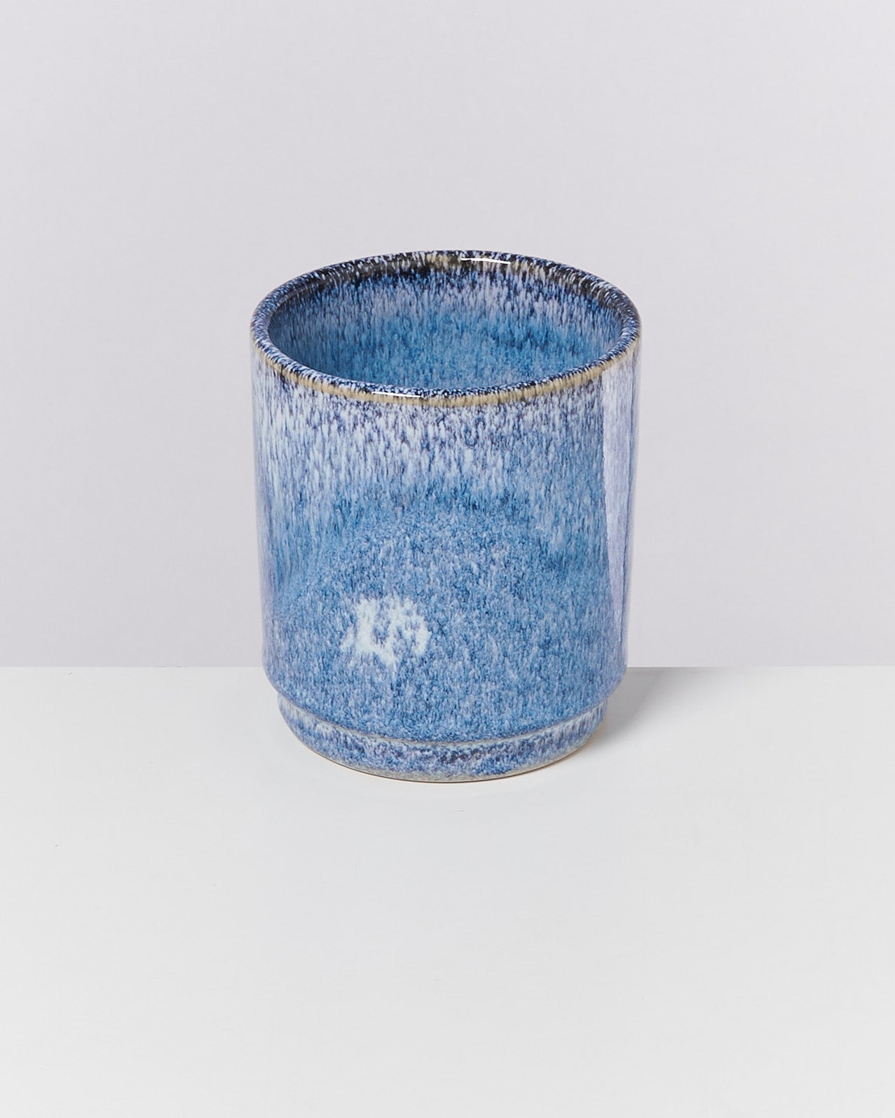 Blauer, zylindrischer Keramikbecher mit gesprenkeltem Muster auf weißem Hintergrund.