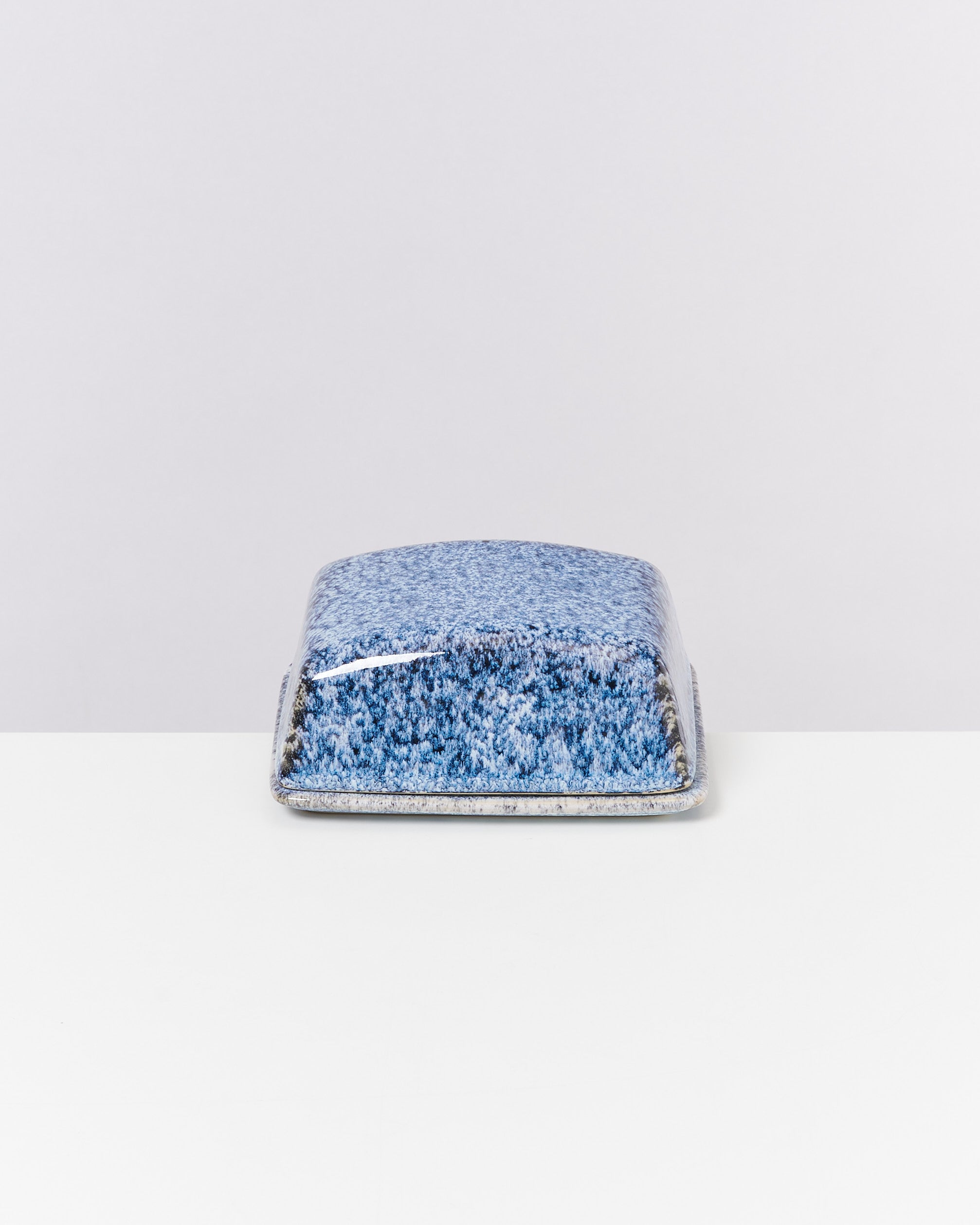 Blaue, quadratische Keramikbutterdose mit gesprenkeltem Muster auf weißem Untergrund.