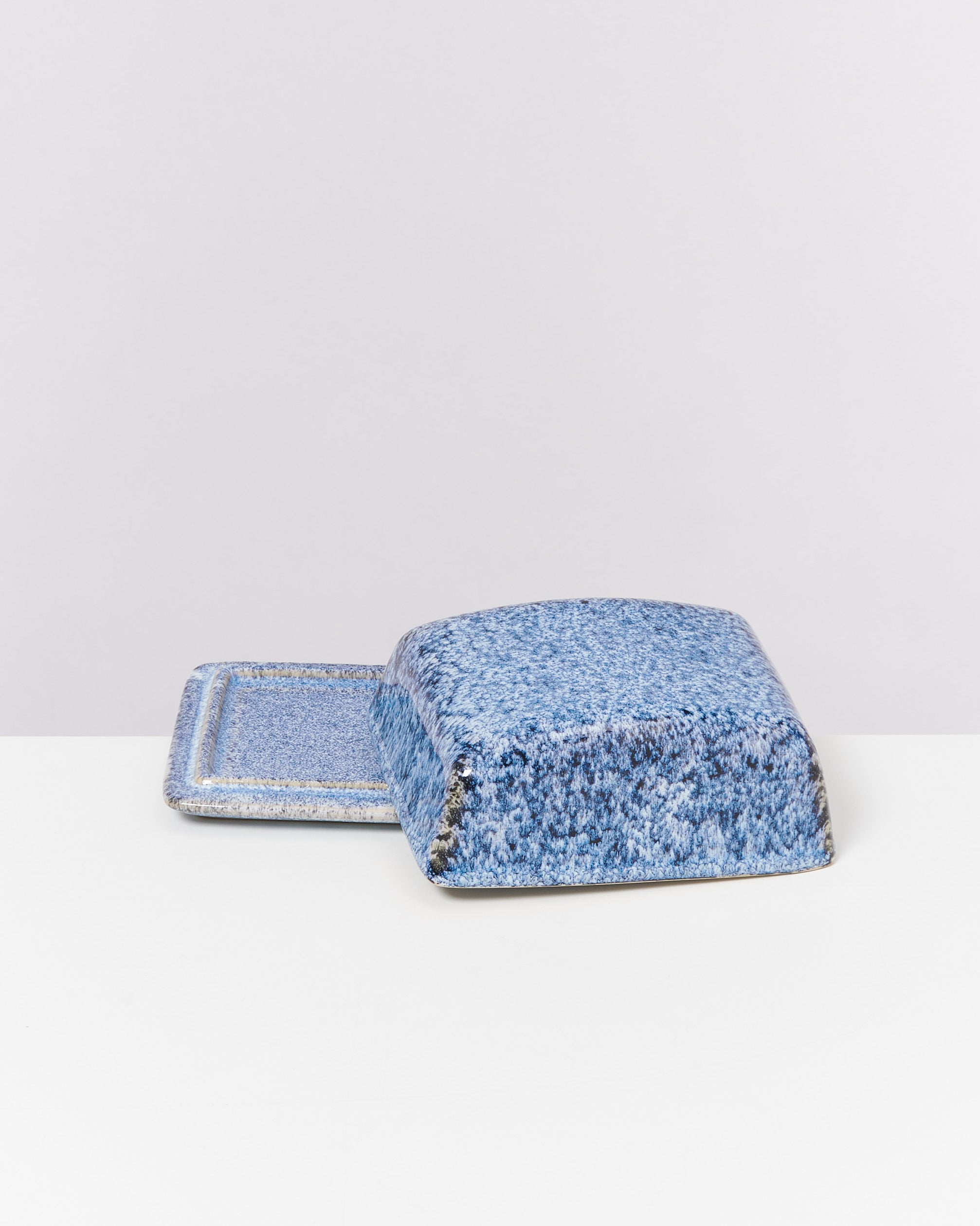 Blauer, rechteckiger Keramikdeckel auf passendem Untersetzer auf weißem Hintergrund.