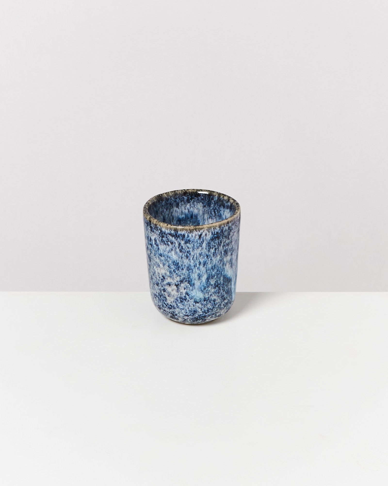 Ein kleiner, blauer, keramischer Becher mit gesprenkeltem Muster auf weißem Hintergrund.