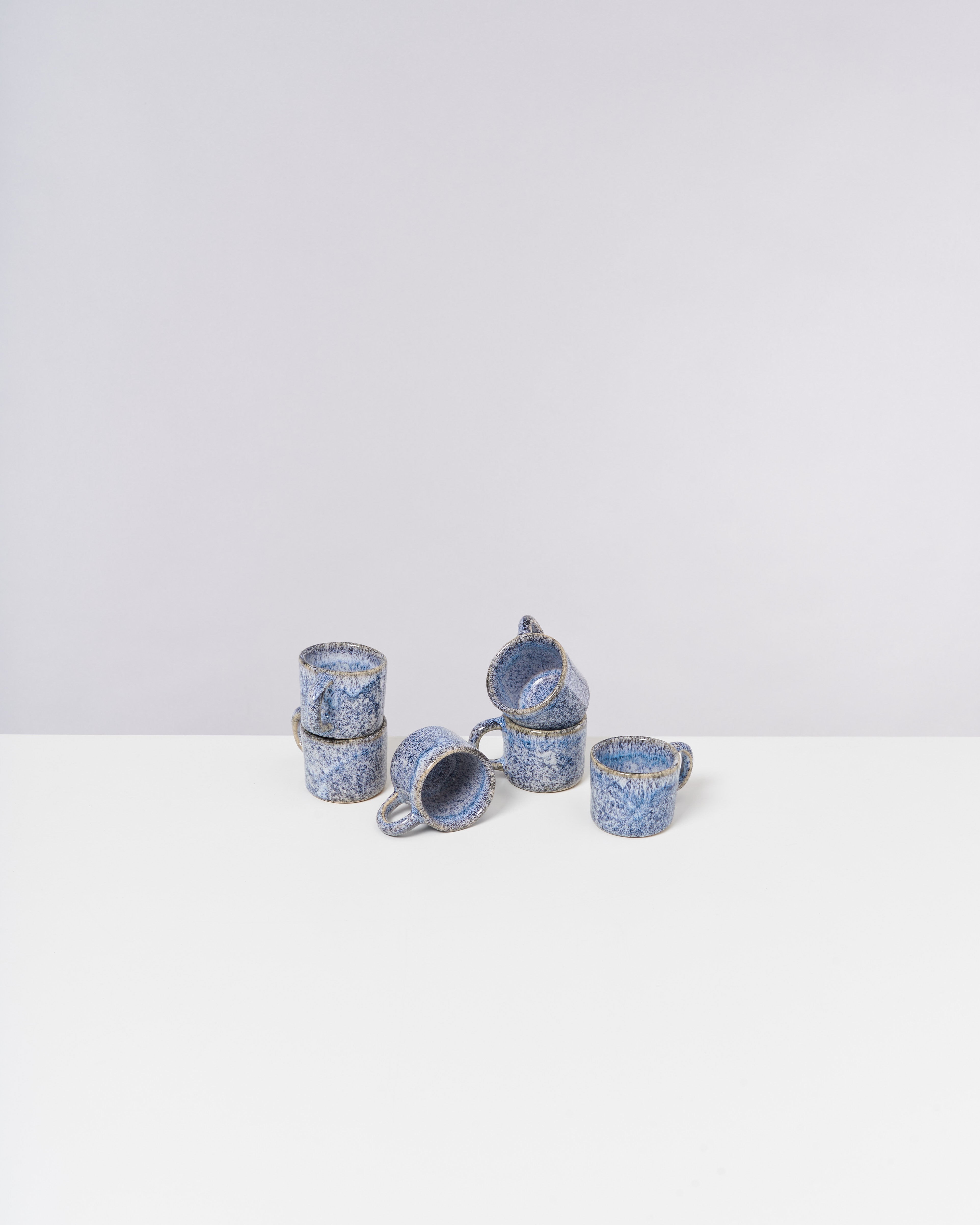 Sechs blaue, gesprenkelte Keramiktassen gestapelt und angeordnet auf einer weißen Oberfläche.