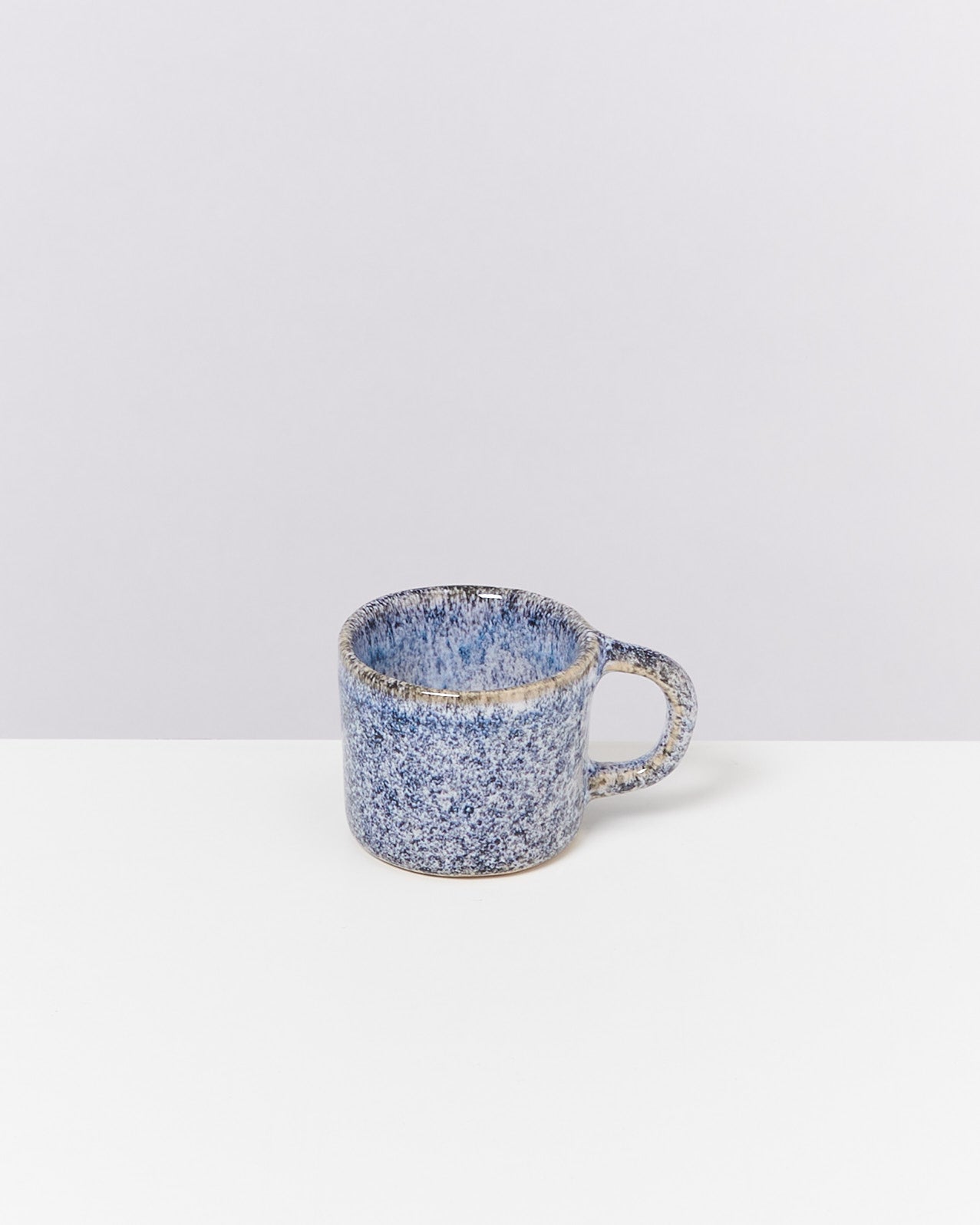 Blaue, gesprenkelte Keramiktasse mit Henkel auf weißem Hintergrund.