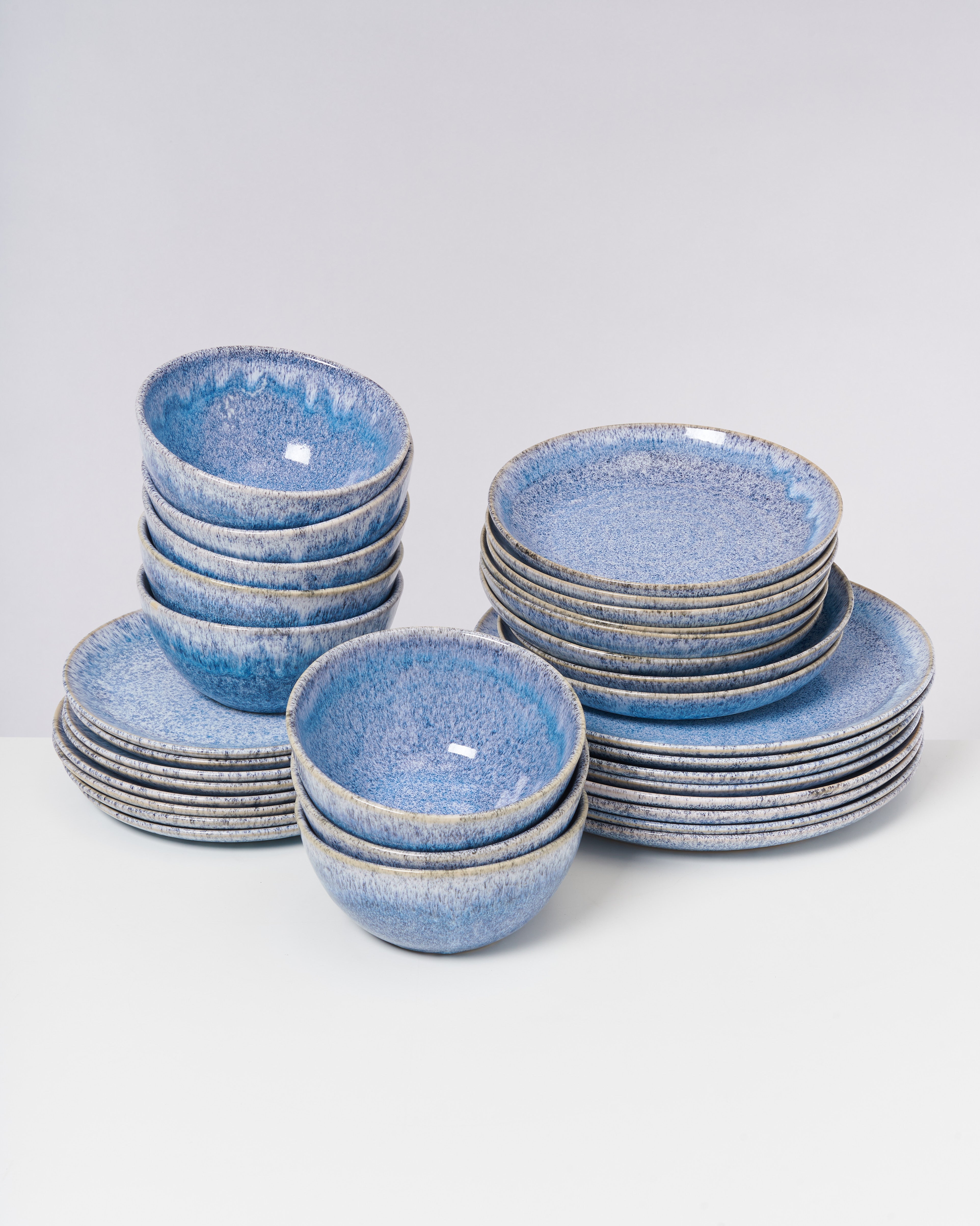 Gestapelte blaue Keramikschalen und -teller auf einer weißen Oberfläche vor neutralem Hintergrund.