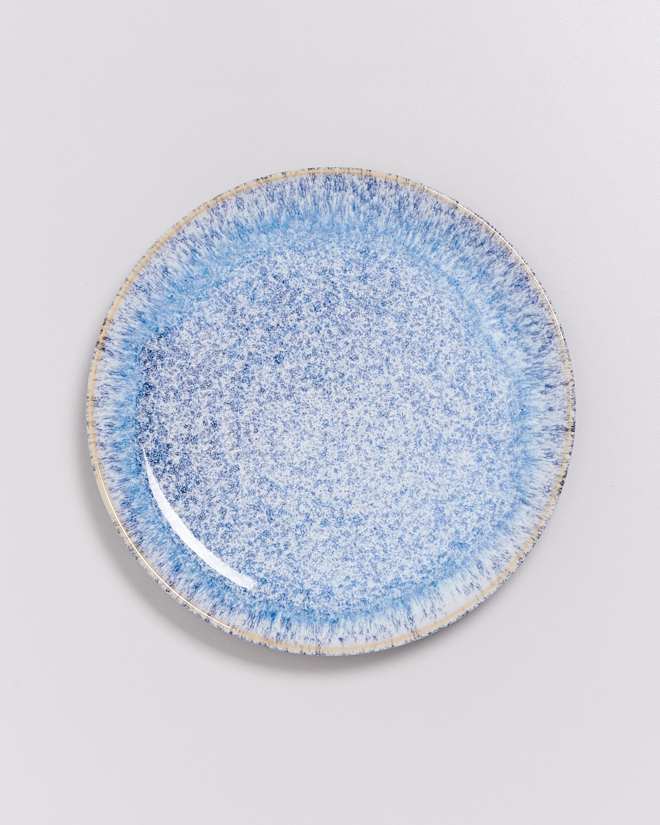 Blauer Keramikteller mit gesprenkeltem Muster auf weißem Hintergrund.