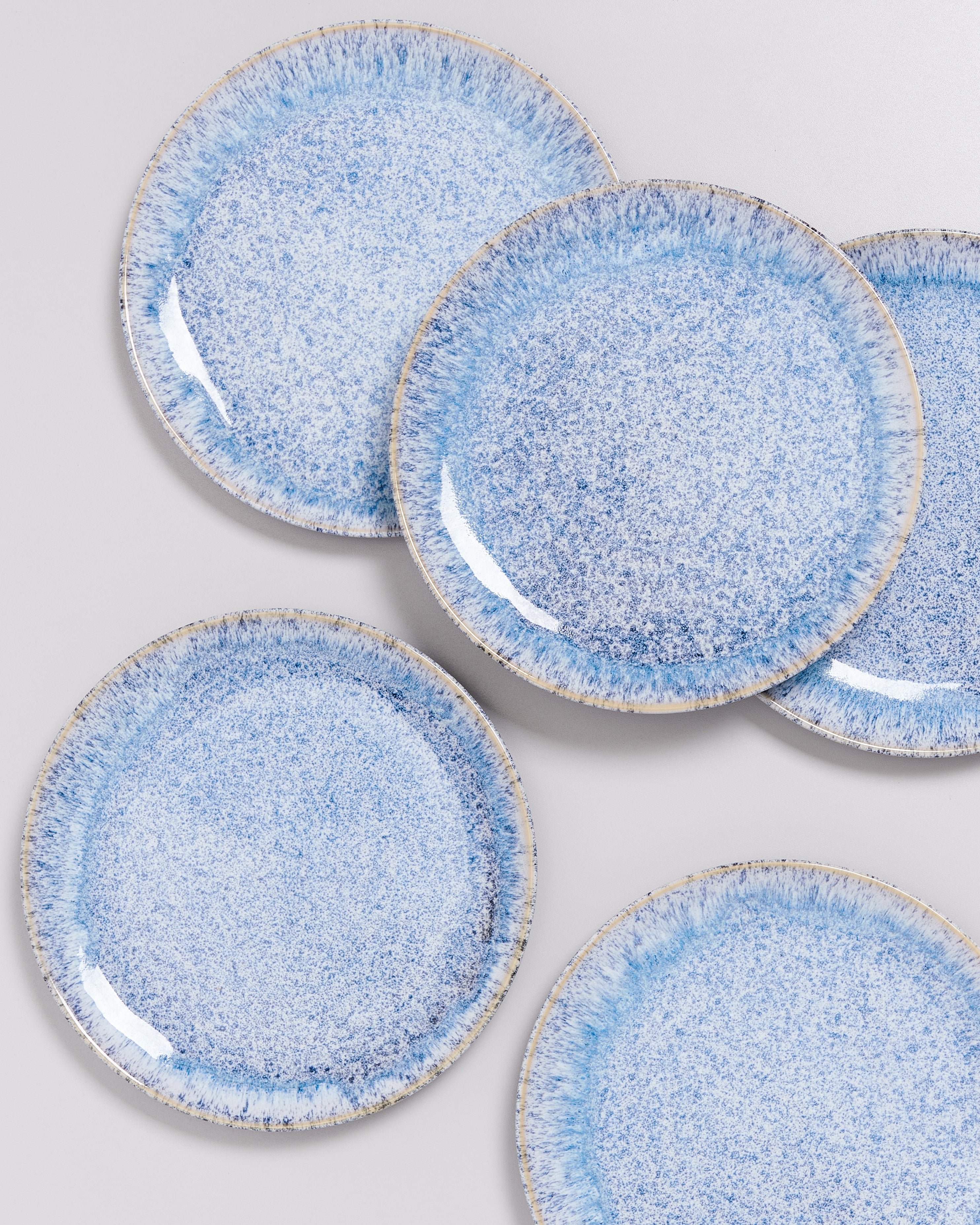 Fünf blaugemusterte Teller mit leicht gesprenkeltem Design auf grauem Hintergrund.