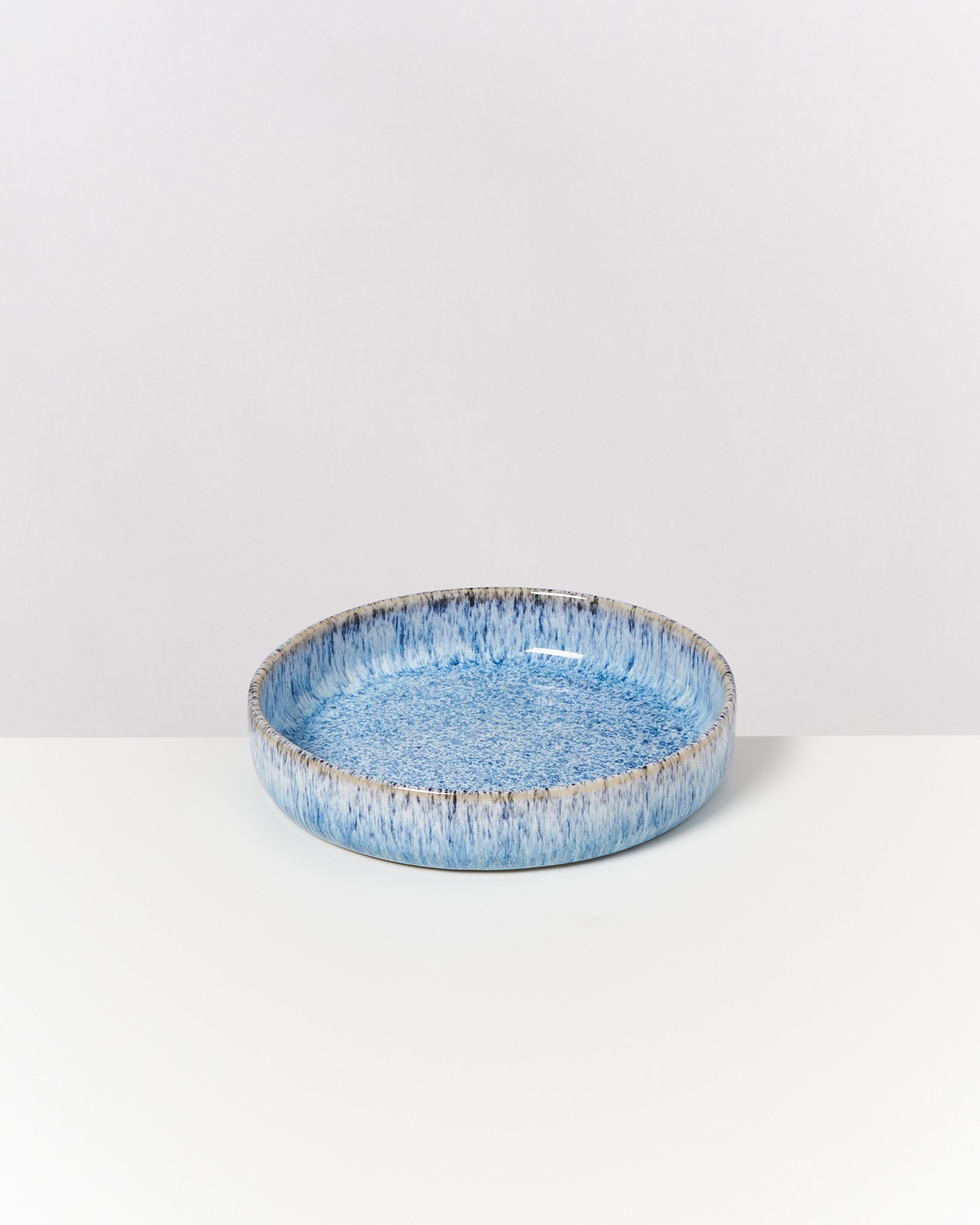 Blauer, flacher Keramikteller mit Mustern auf weißem Hintergrund.